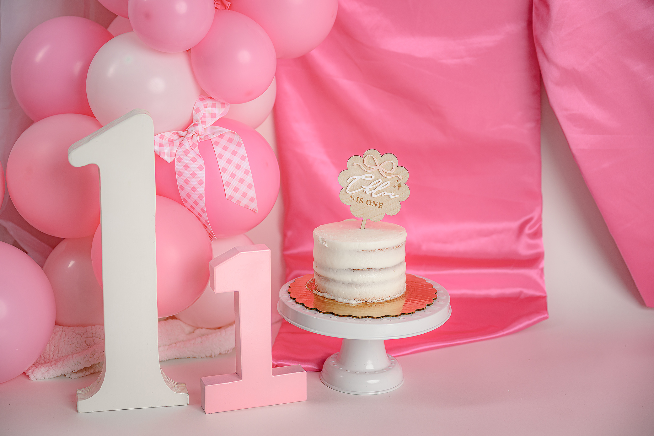 Close-up image of a cake smash cake that’s multi layered with a cute cake topper and two large number ones in a baby milestone session