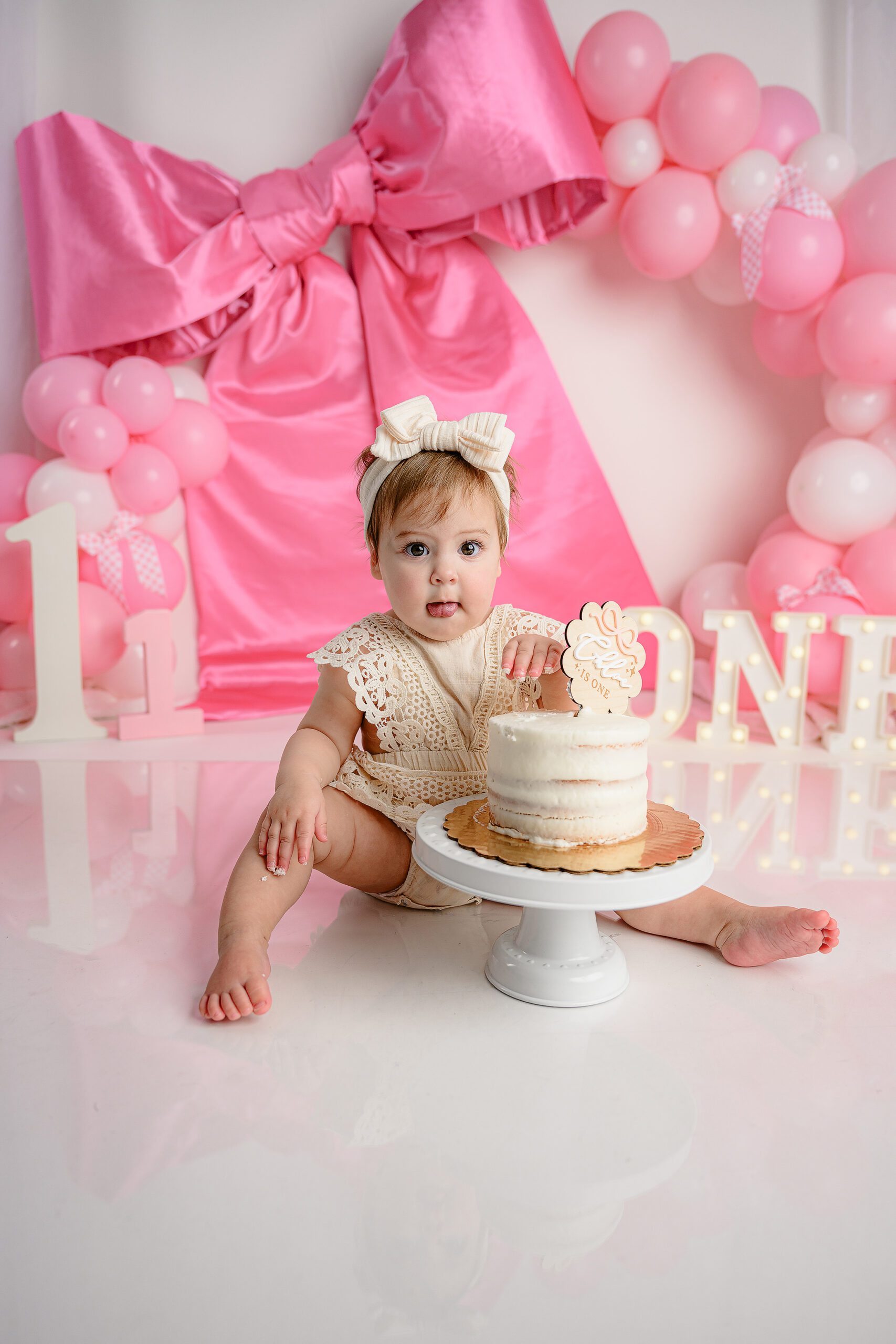 Little girl smashing her cake during her one year milestone session and a pink and white set up with the theme girls just wanna turn one