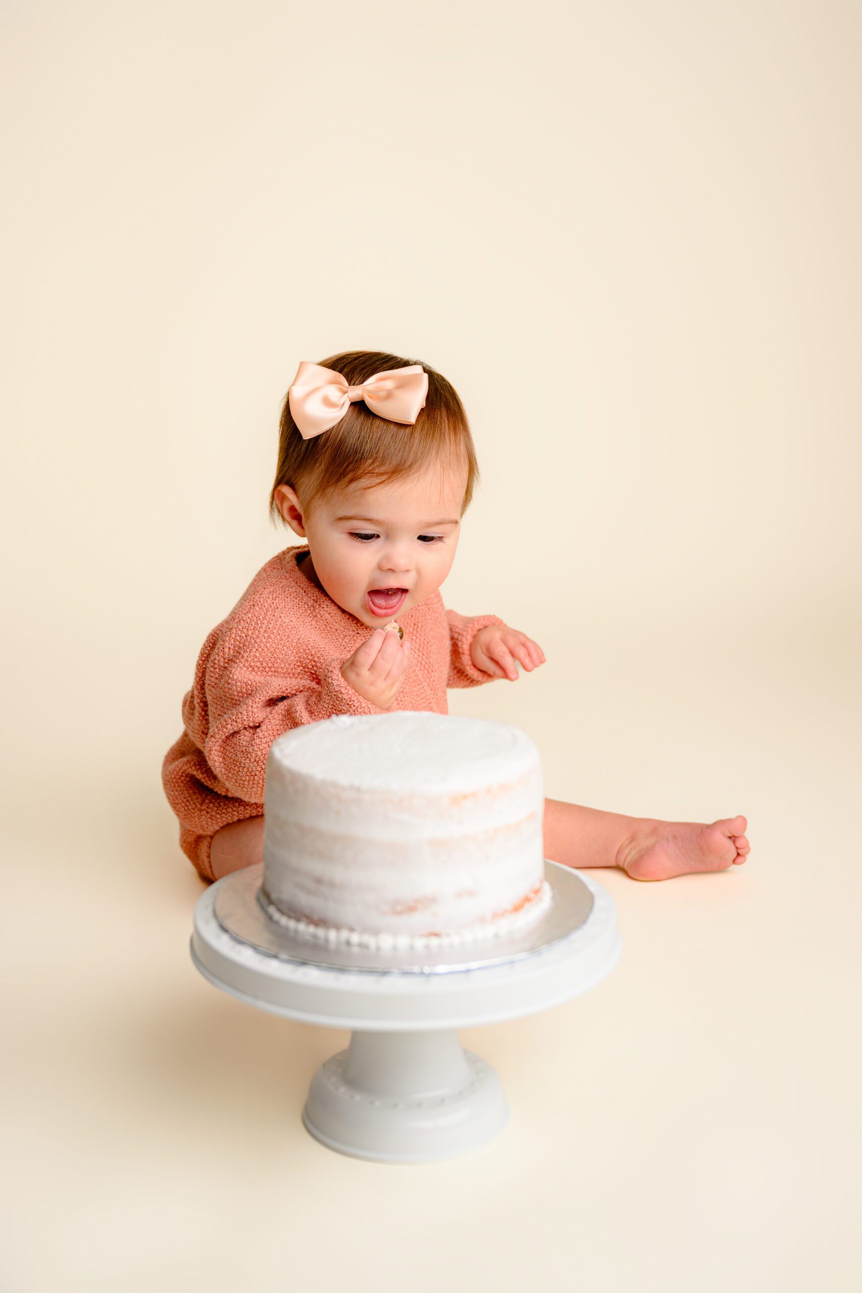 Happy one-year-old baby girl taking. a bite of her cake during her smash milestone session