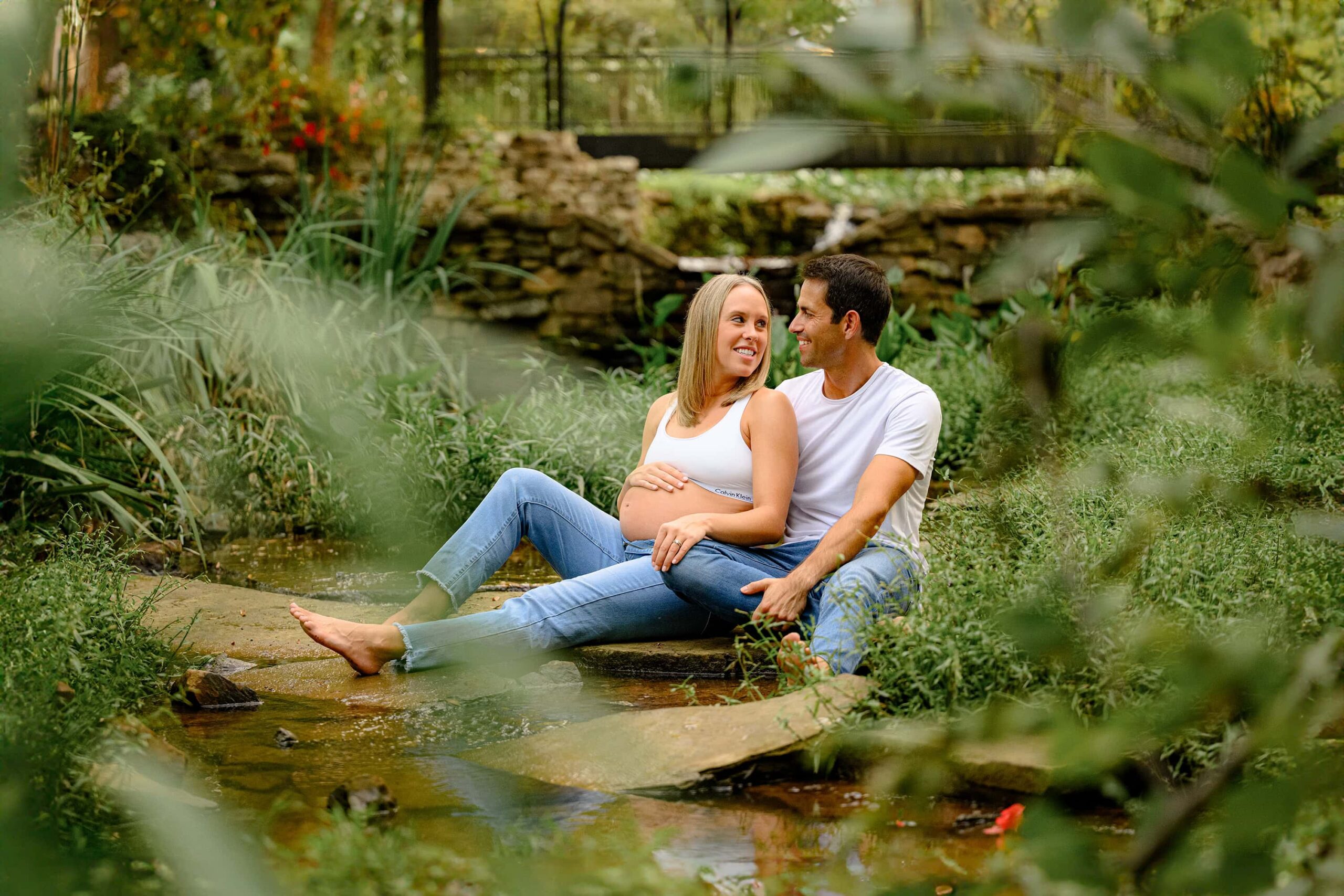 Charlotte NC expecting couple sits serenely together during their bump to baby maternity session in a local garden area garden. both are dressed simply to make sure they stand out during their session