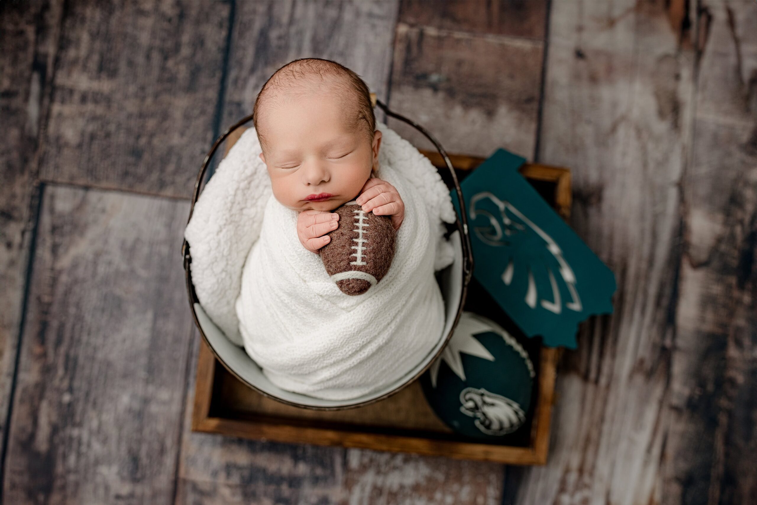 fly eagles fly is all this little newborn boy is dreaming about during his newborn photoshoot while wrapped in white surrounded by eagles gear