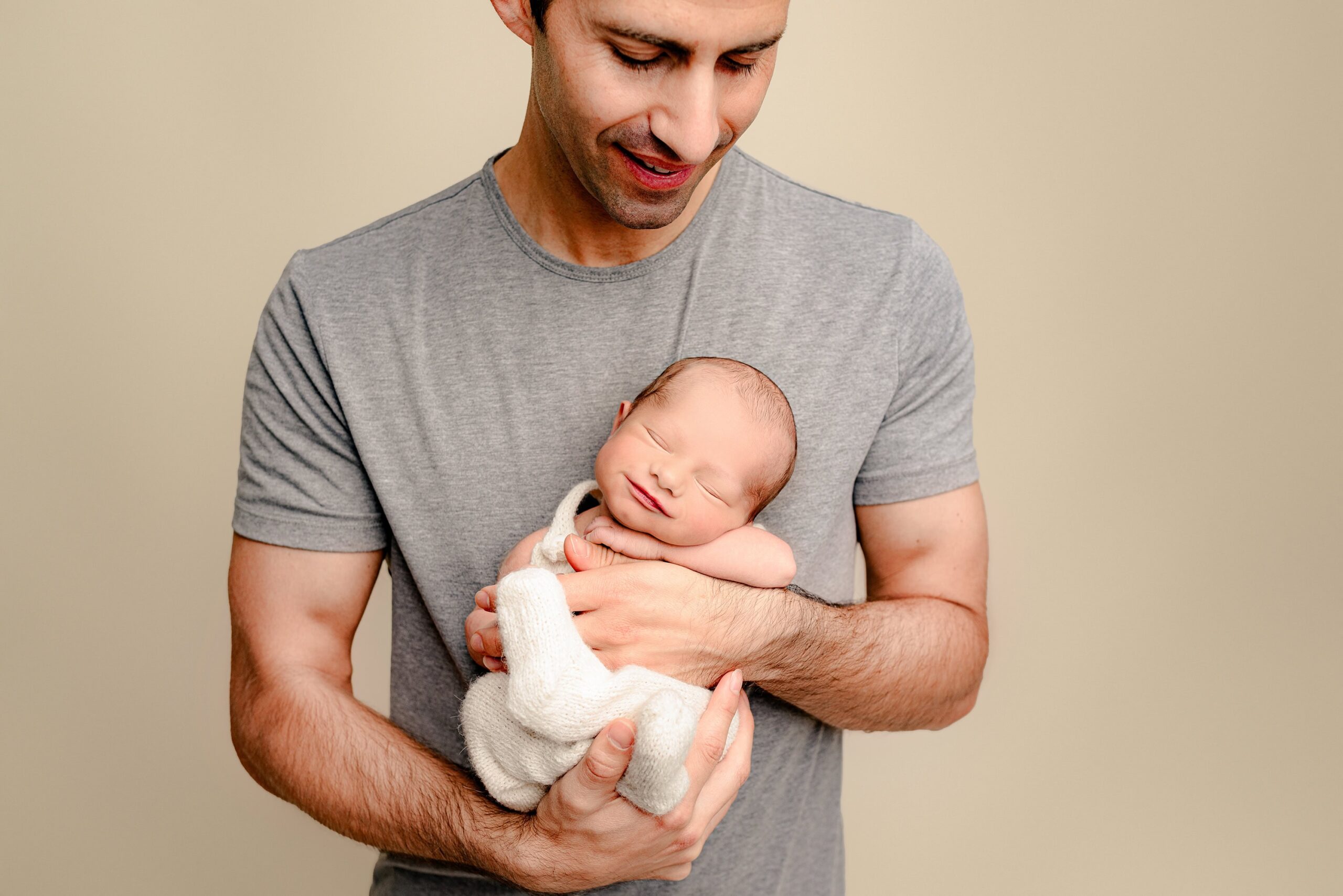 baby boy dressed in white smiles in Charlotte area dad's arms during his maternity to newborn waxhaw studio photo session