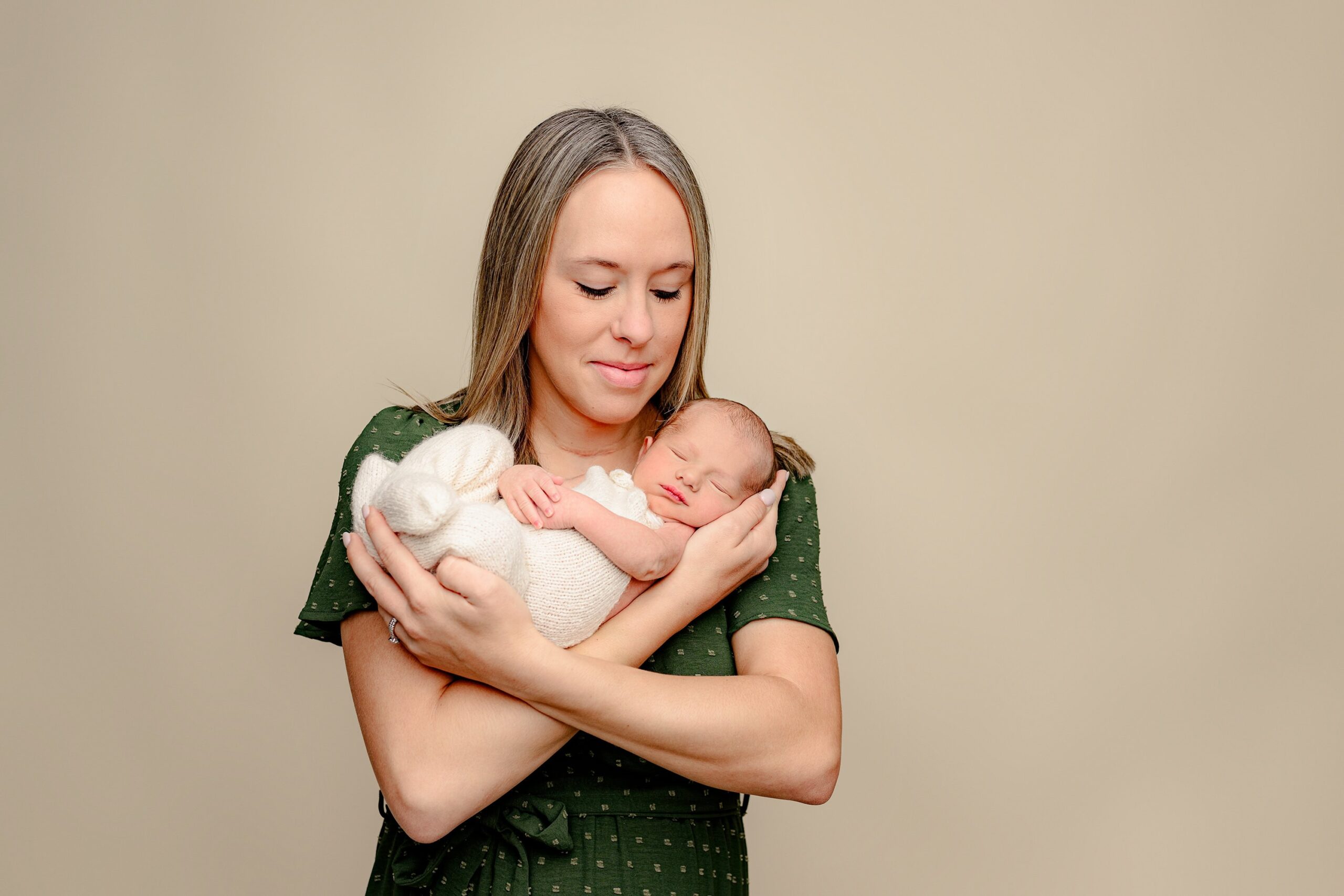 mother dressed in green looks down sweetly at her newborn son cradled in her arms during his newborn photography session in the charlotte nc area