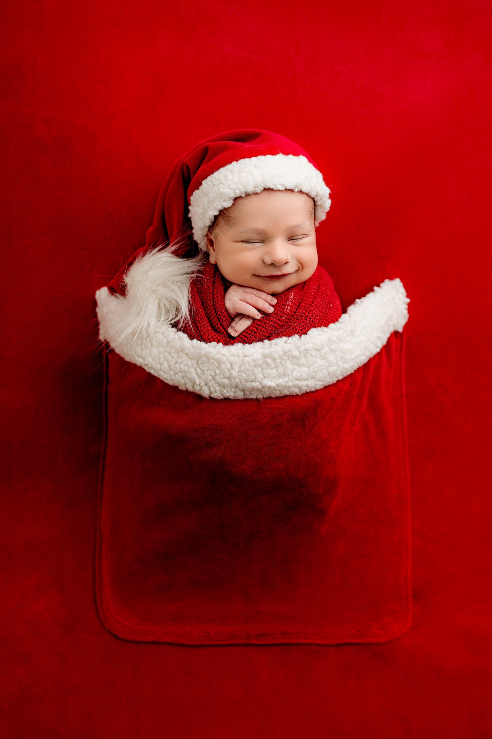 newborn boy wrapped up in a set that looks like Santas pocket with a little newborn hat smiling in his bump-to-baby photo session in the charlotte area studio