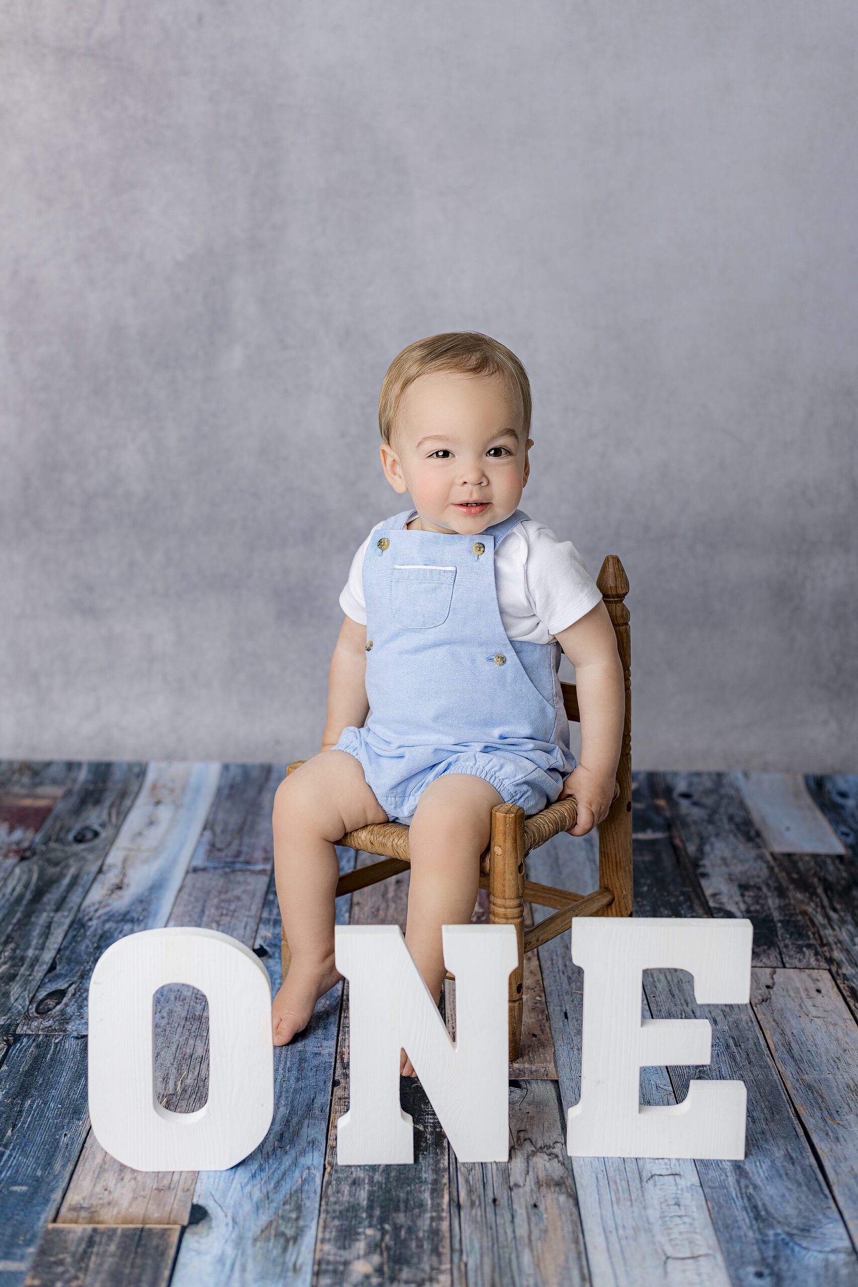 charlotte area boy sits in chair dressed in blue overalls and white shirt with O N E letters in front of him