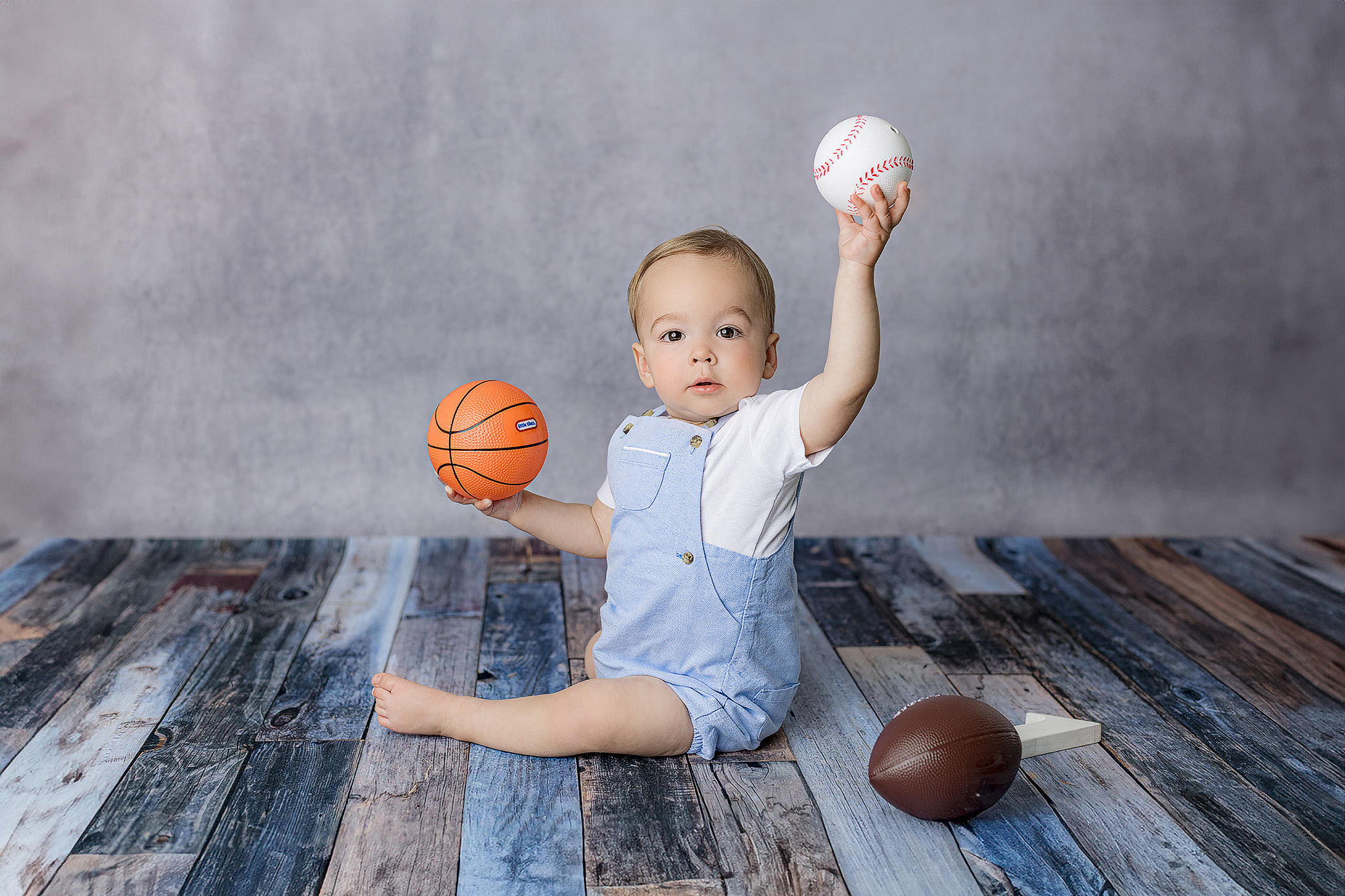 little boy holds his fun balls from home while playing and interacting with photographer during his one year old studio milestone session