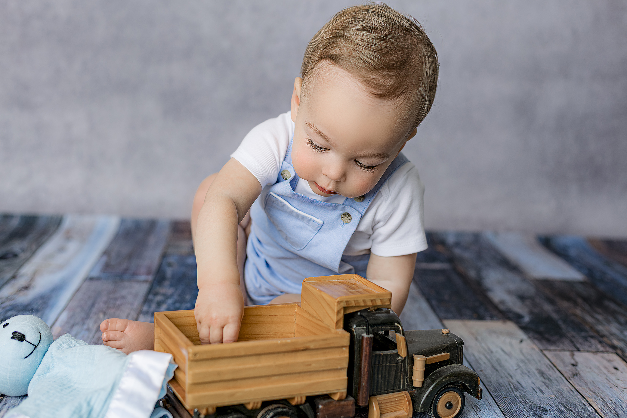 look at those amazing eyelashes on this little boy while he plays with a wooden truck during his milestone studio session in the charlotte nc area
