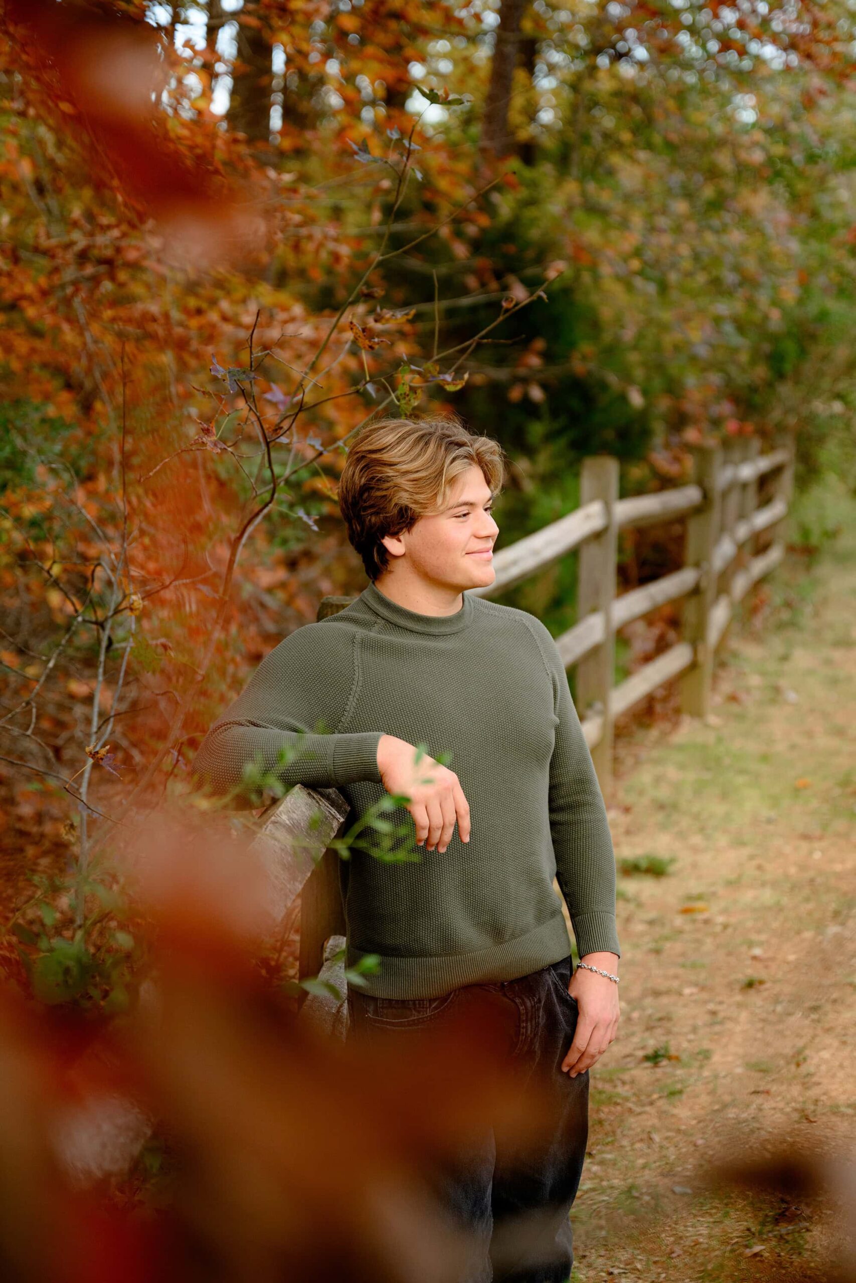 CHS grad laughs off camera while standing by a fenceline during his fall senior portrait session in a waxhaw area park