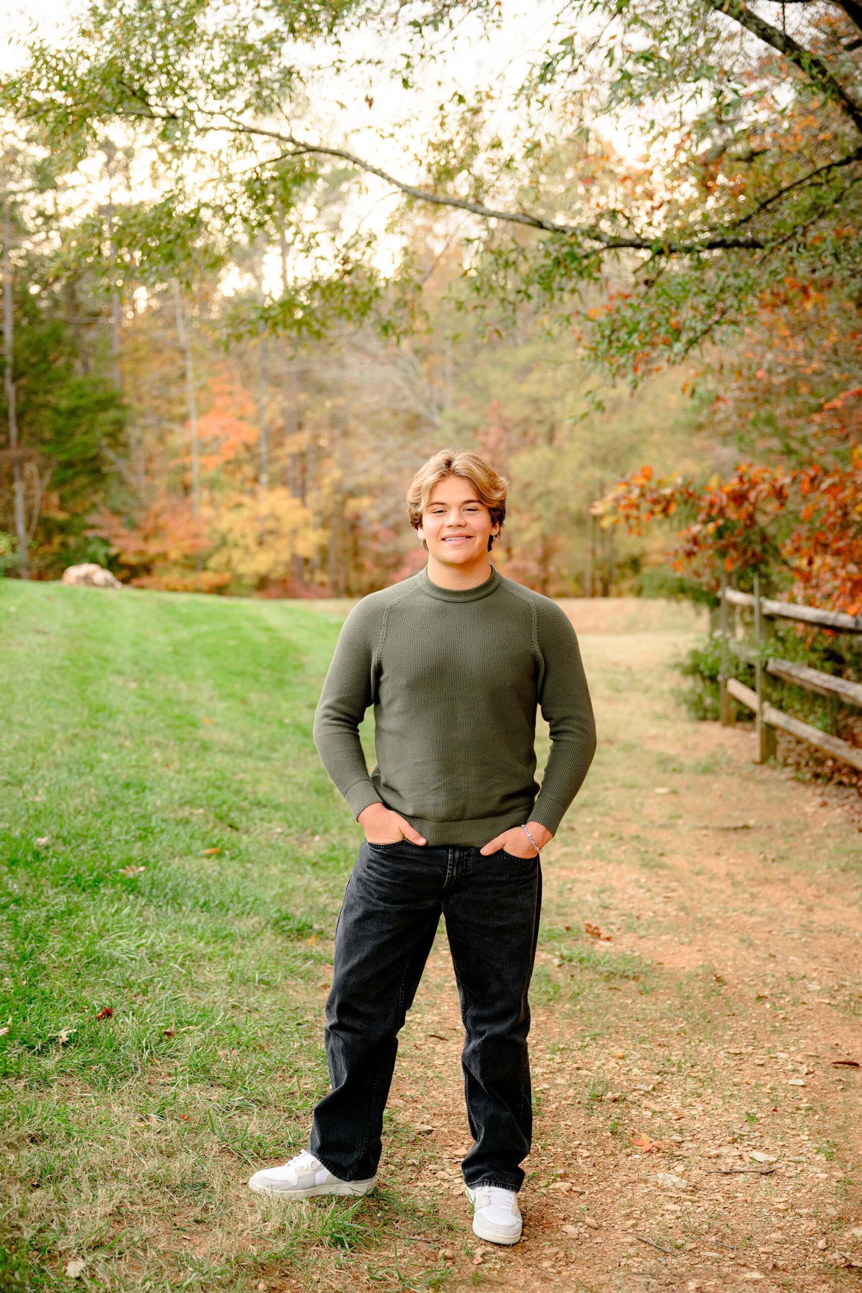 CHS Class of 2025 grad stands with his hands in his pockets for his senior photos while wearing a green shirt and dark pants during his stylish portrait session