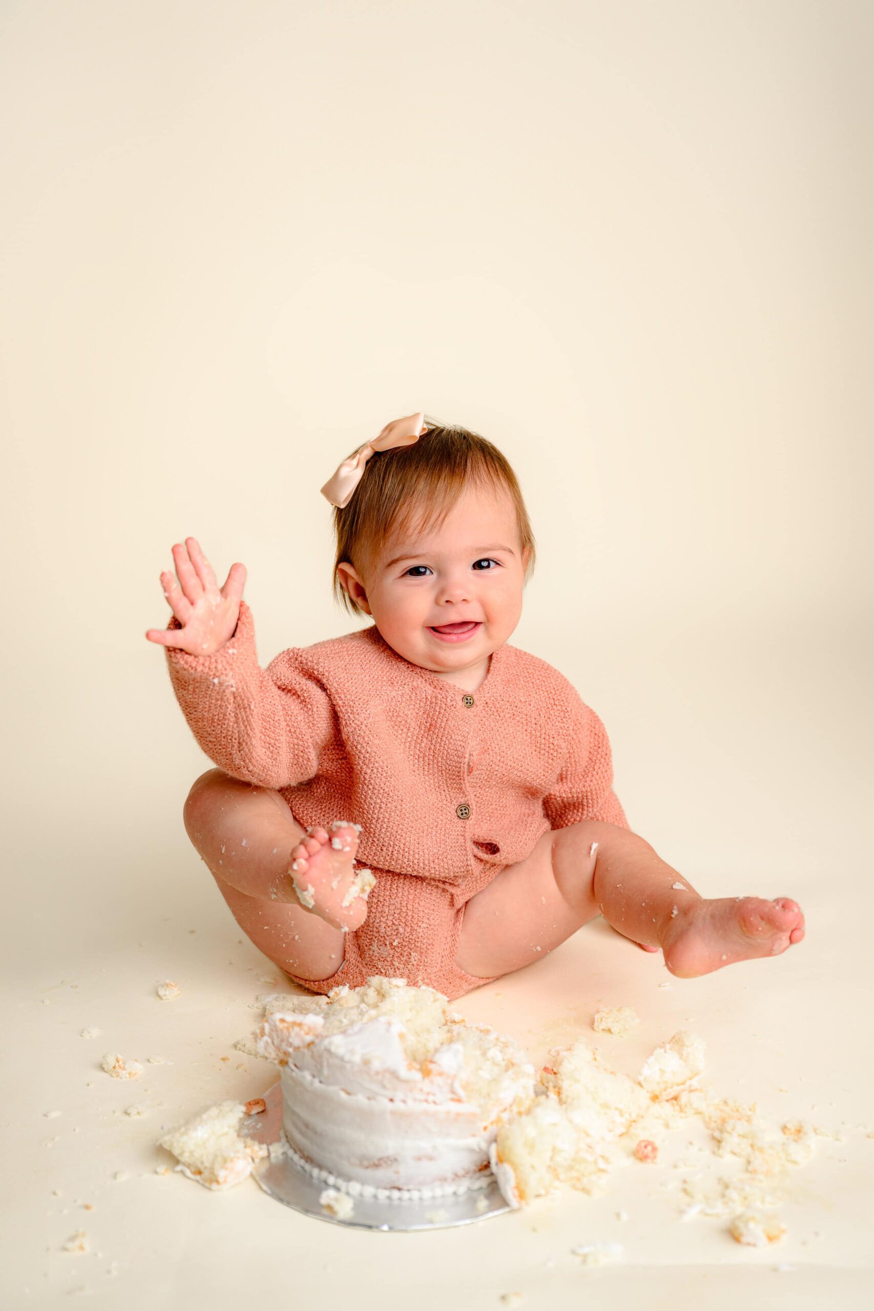 Happy one-year-old baby girl sitting beside her cake during her smash laughing joyfully during her simple cake smash milestone session