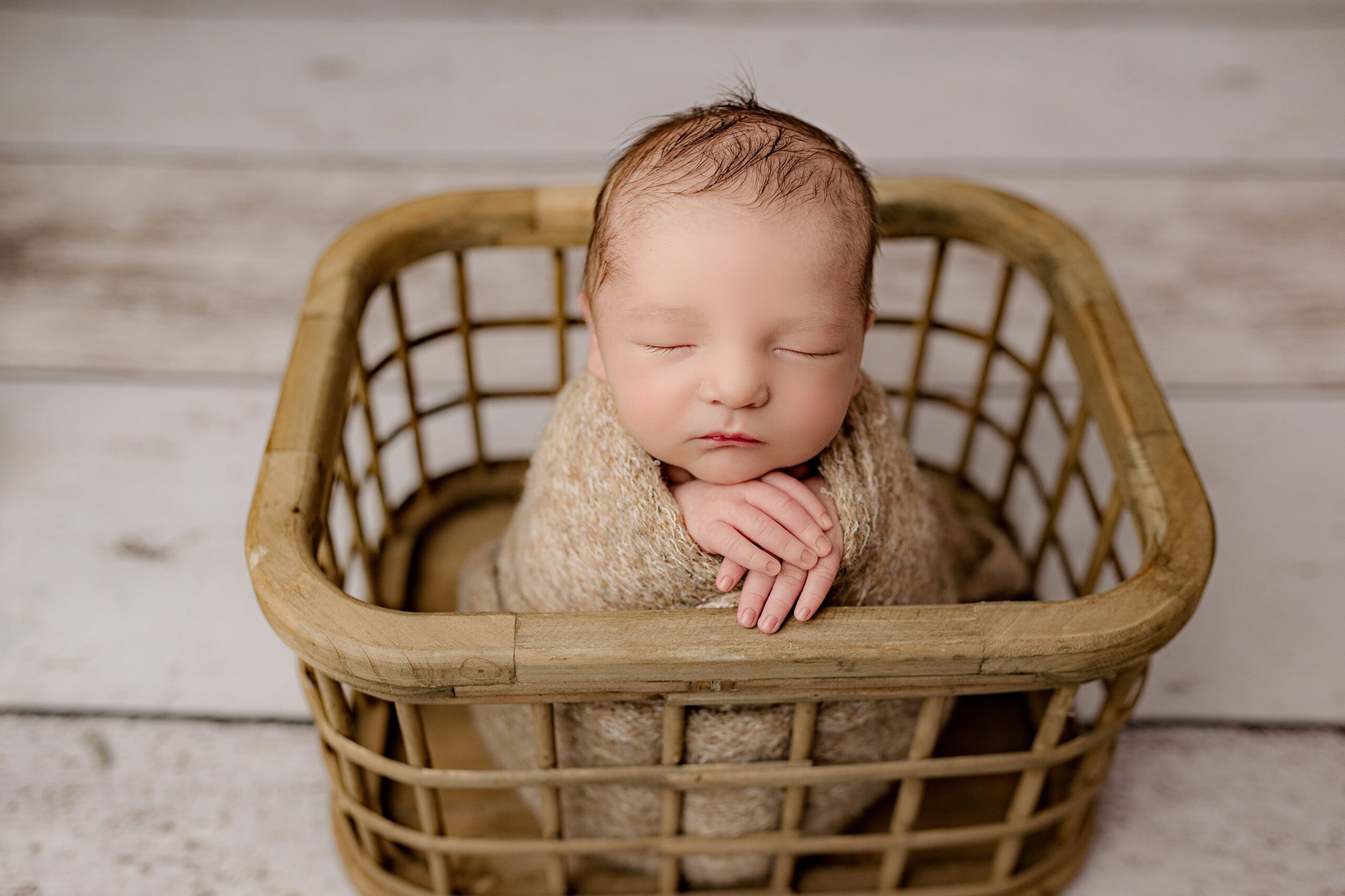 newborn baby wrapped in basket posed with hands on edge of basket during his lifestyle newborn session in the south charlotte nc area