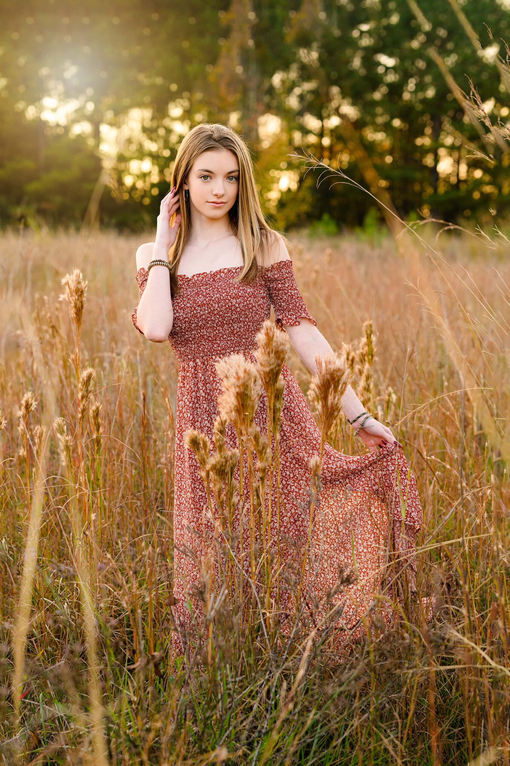 senior girl is backlit by the sun holding her dress with her hand and her hair back with her other hand