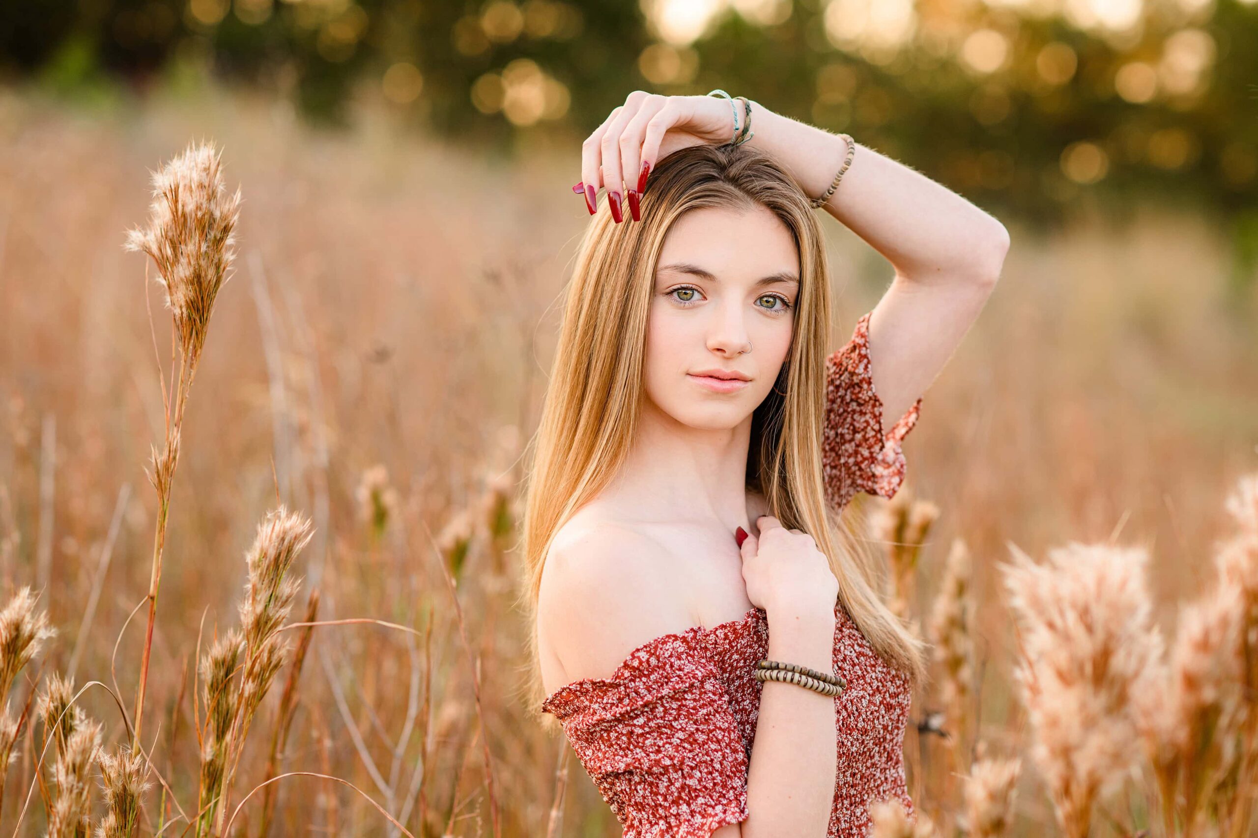 senior dressed in rust color off shoulder dress with hands close to face and her red nails showing