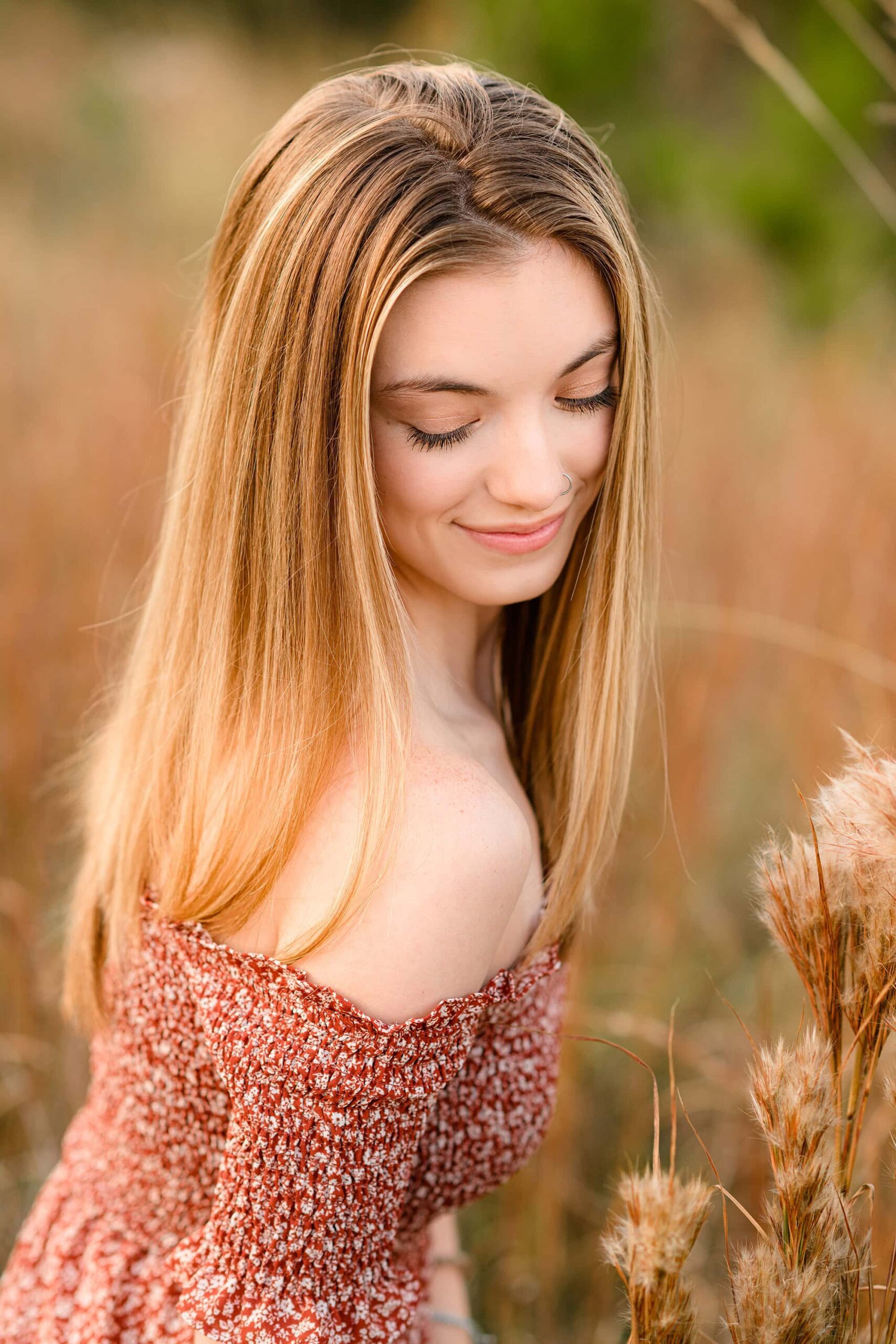 female senior looking down at her shoulder wearing a rust off the shoulder dress