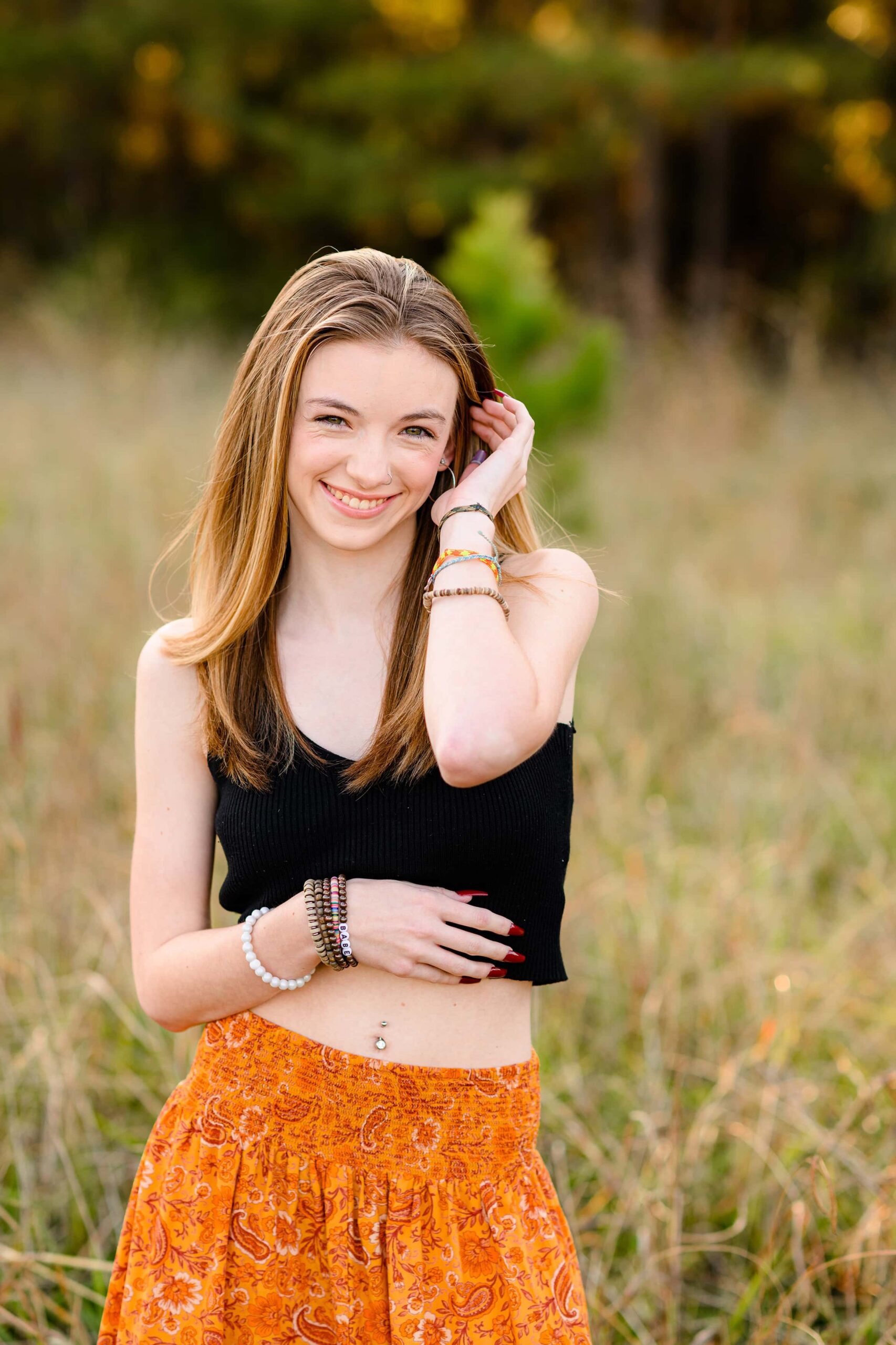 grad tucks her hair behind her ear as she stands in a field wearing a crop top and skirt