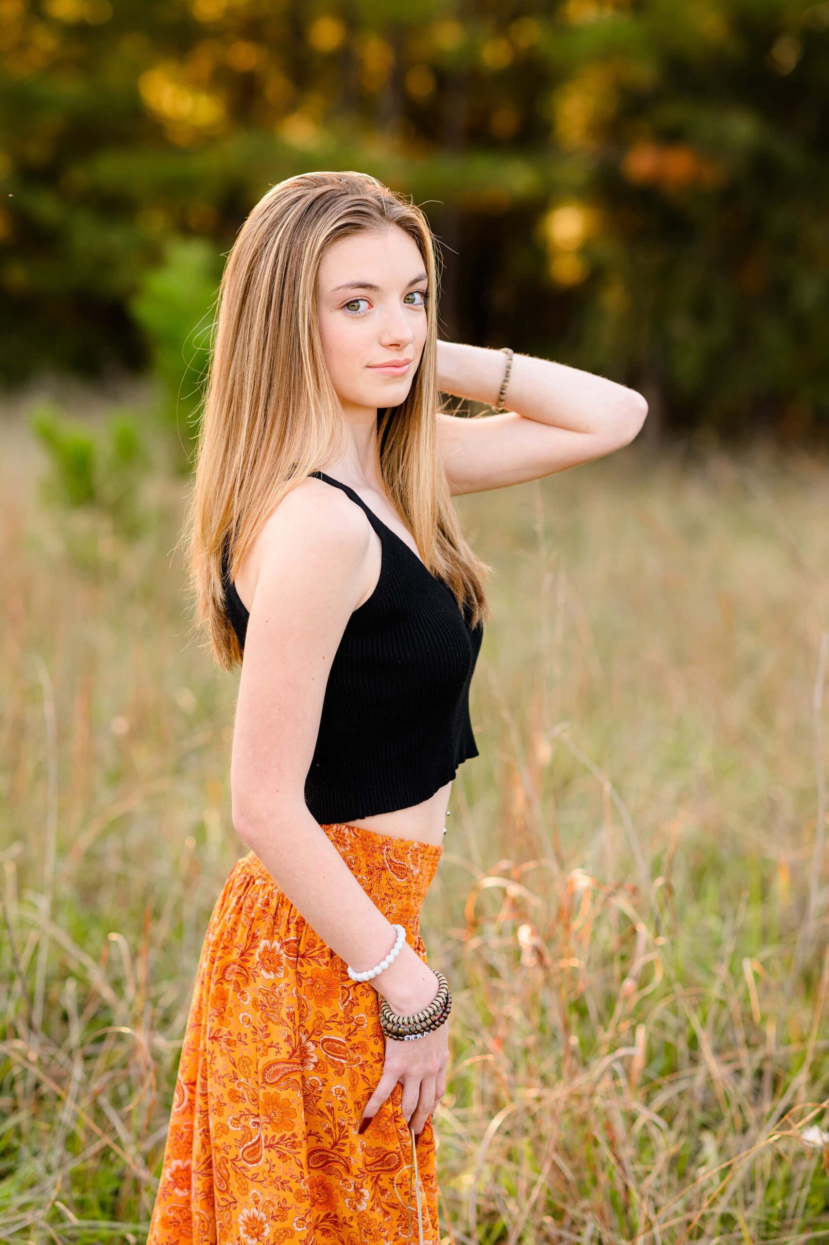 long hair senior girl wearing a black crop top and orange skirt with hand up by her head