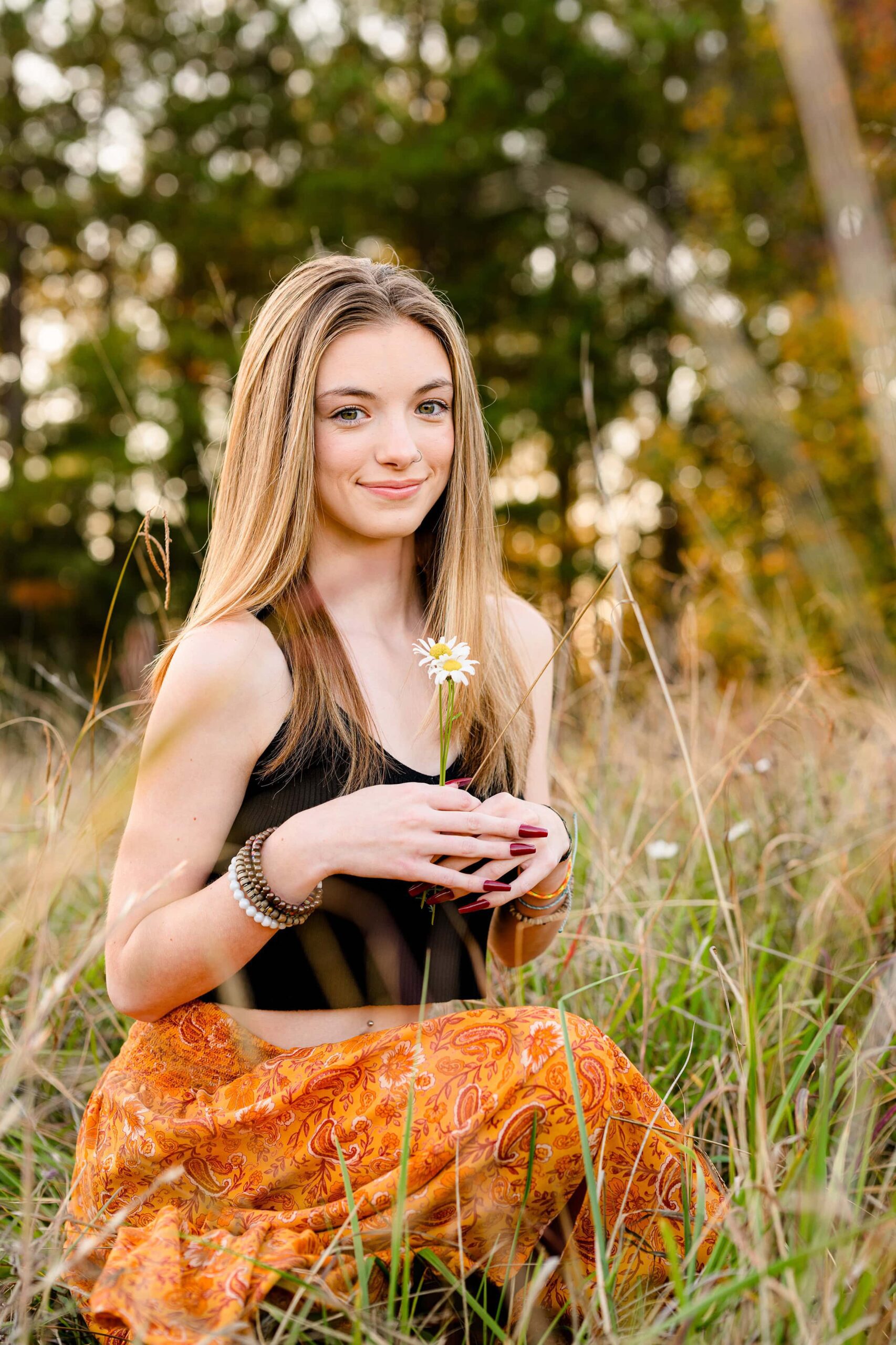 senior girl wears a black shirt and orange skirt holding a small bunch of flowers