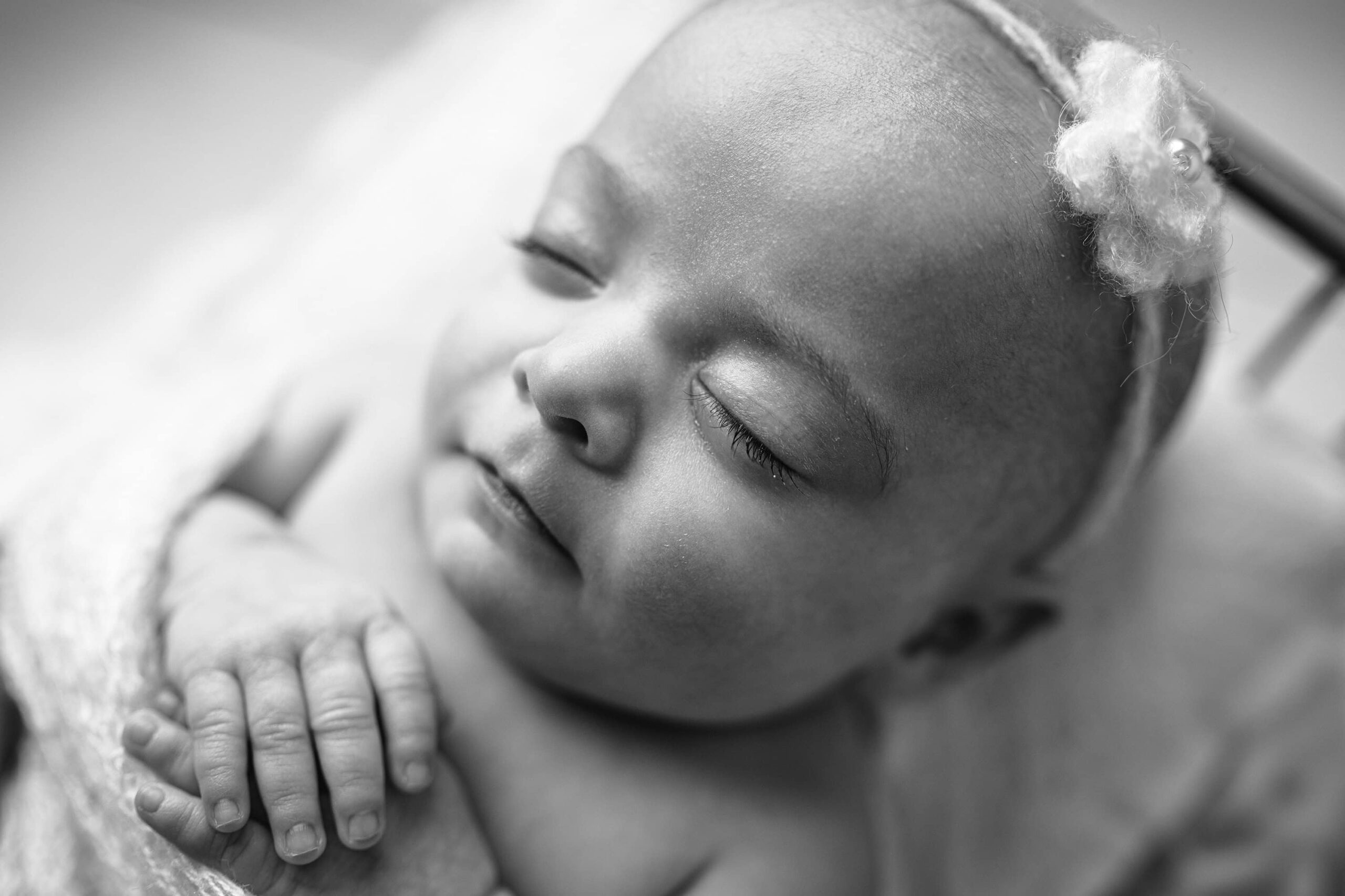 Black and white portrait of a newborn girl, capturing her full face and tiny hands resting on her chest.