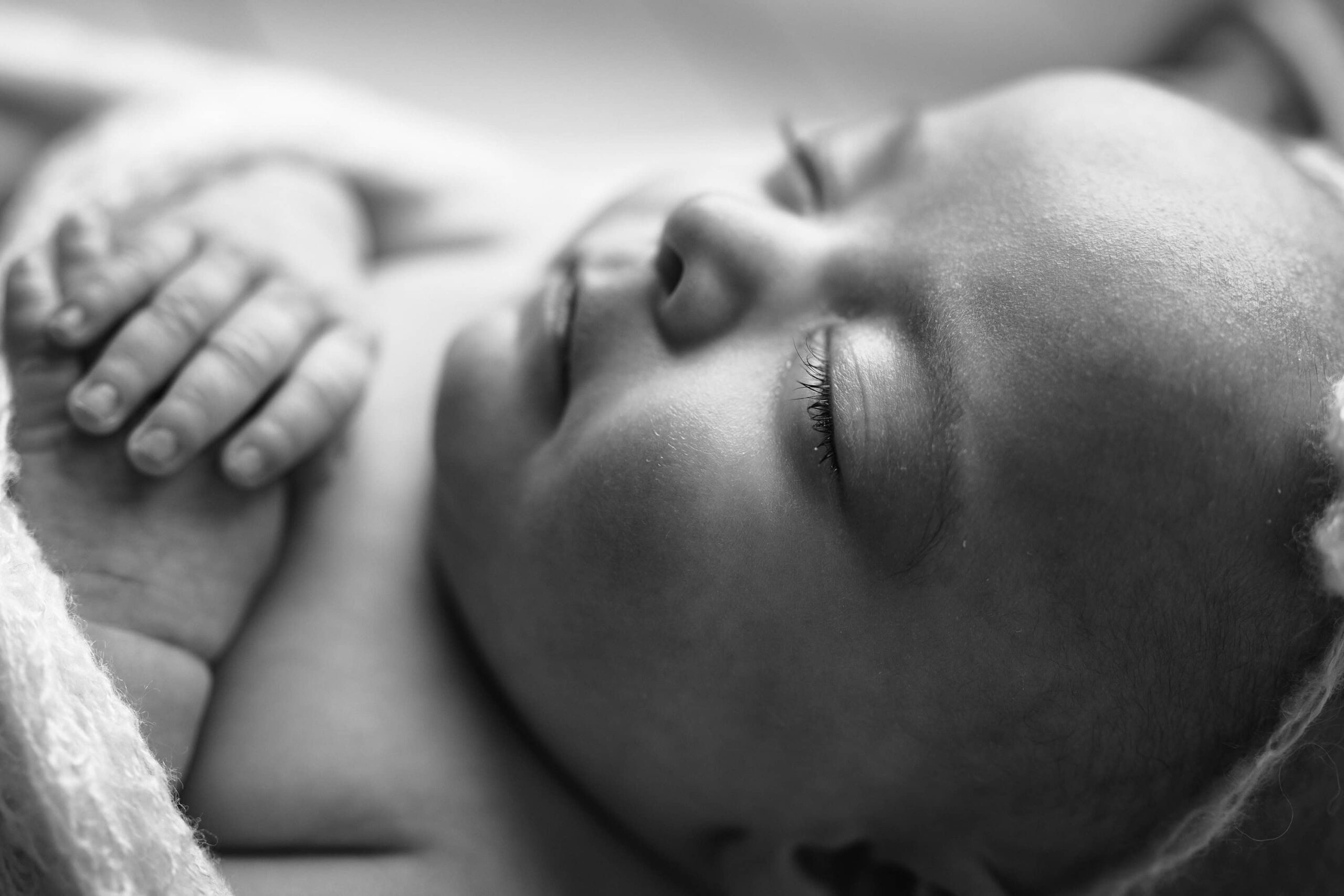 Soft black and white detail photo highlighting the newborn’s long, wispy eyelashes.