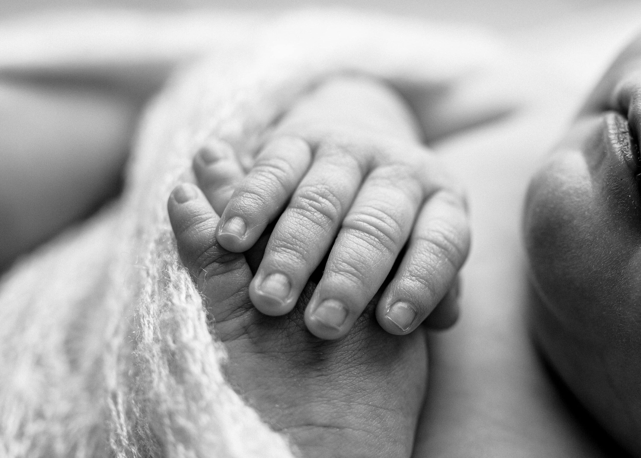 Black and white close-up of the newborn’s tiny fingers curled gently in her hand.