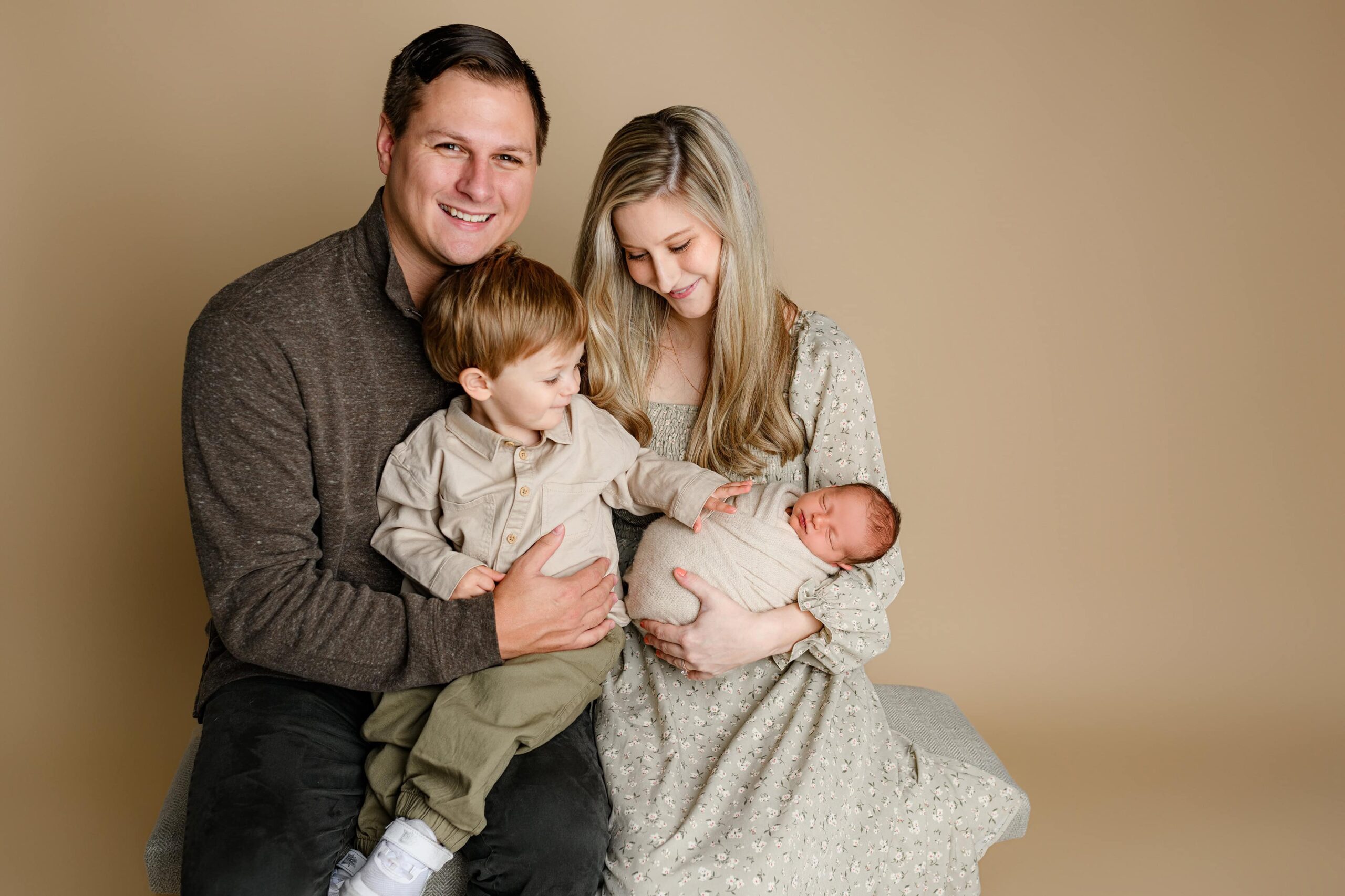 Lancaster, SC family together in a Waxhaw studio—mom in a cream dress holding the newborn, dad holding their toddler son, who touches his baby brother’s nose.