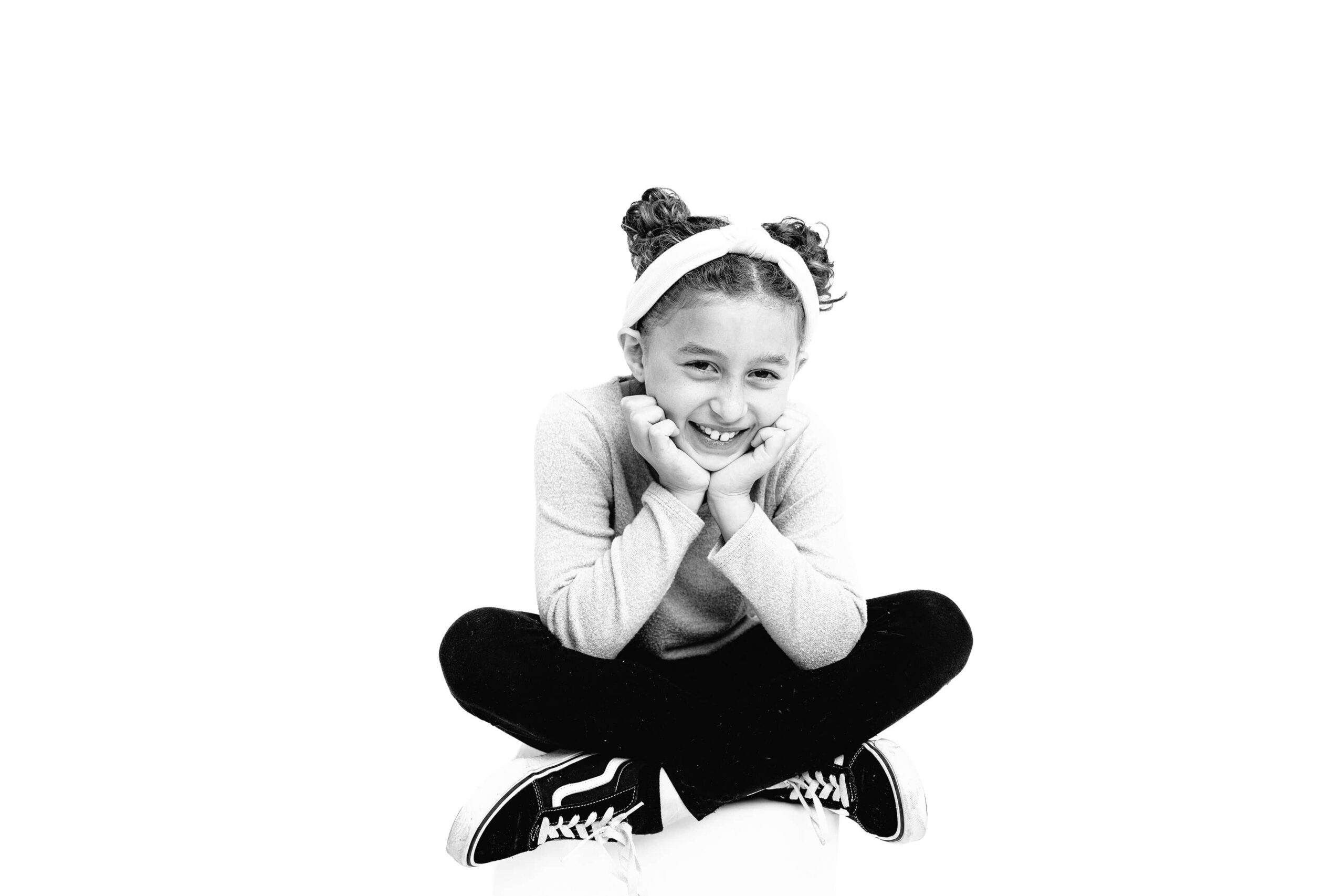 black and white high contrast image of a ten year old girl sitting cross legged with both hands on her cheeks laughing