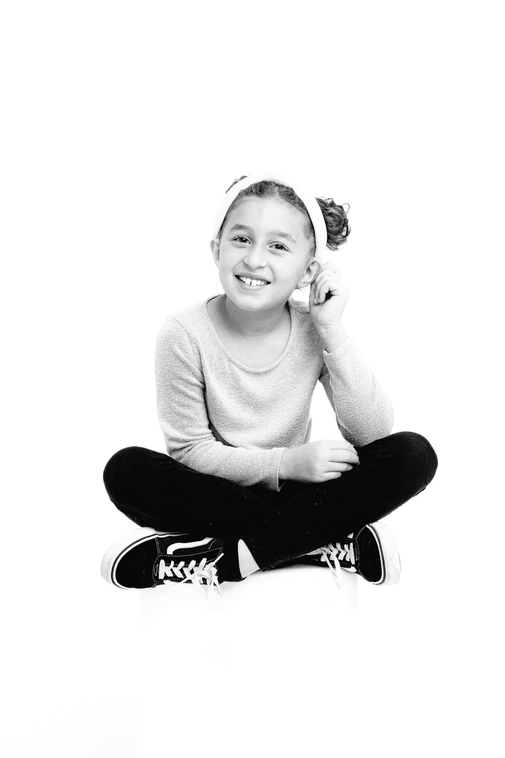 black and white image of a ten year old girl sitting cross legged tugging her ear