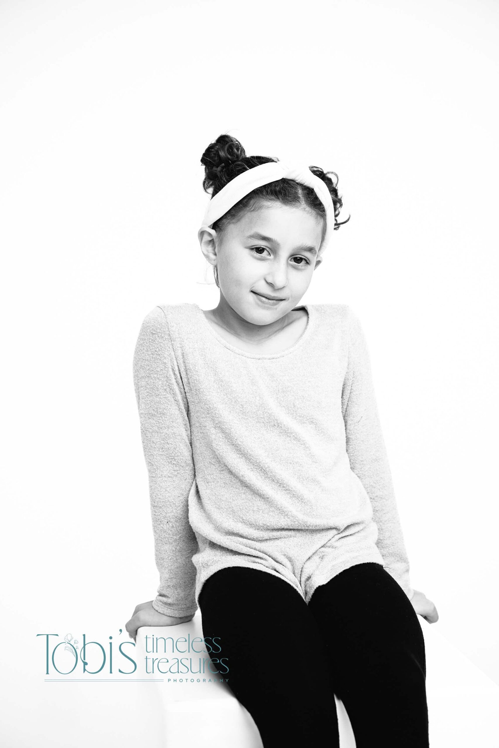 black and white milestone photo of little girl sitting on a stool smiling softly