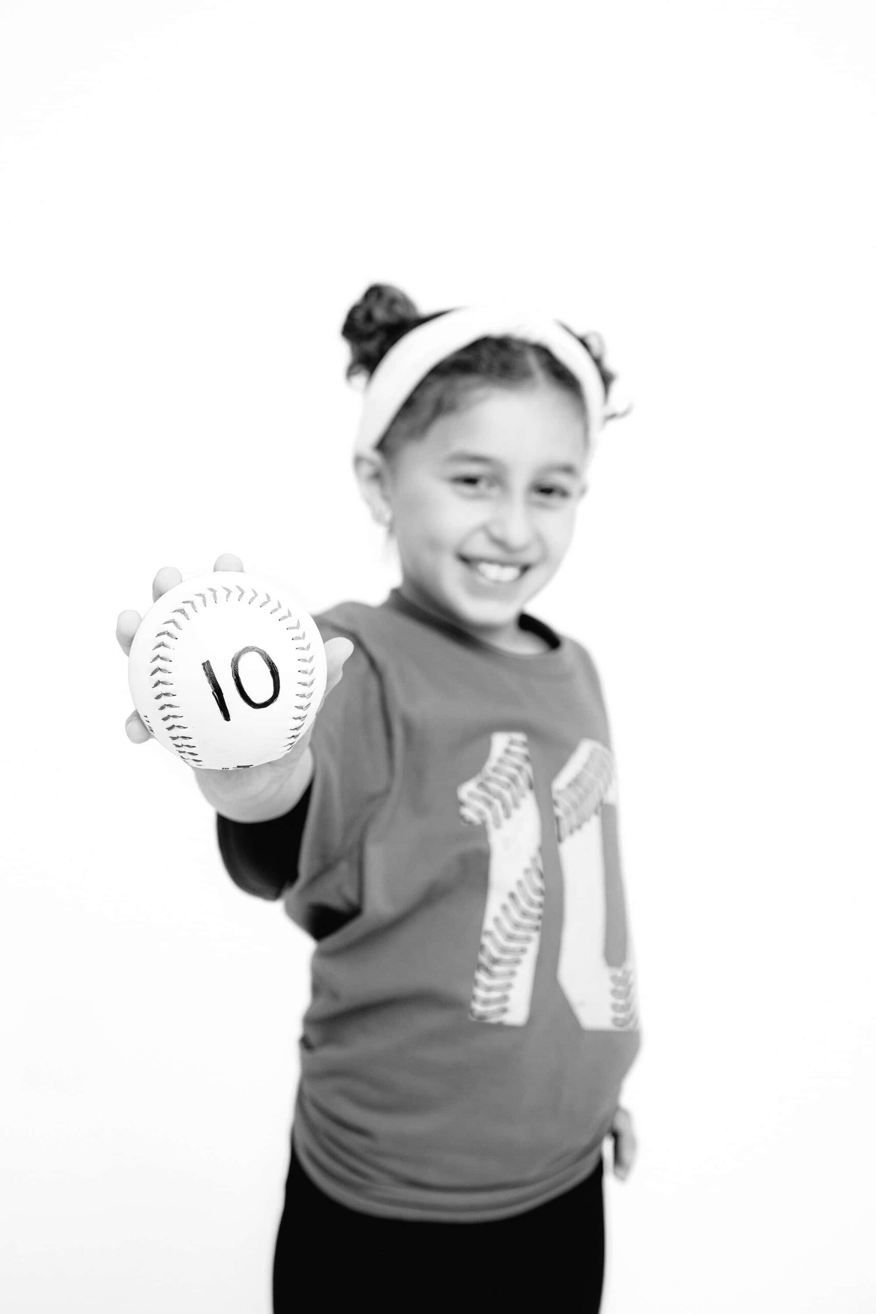 black and white image of a girl holding out a softball wearing a number 10 t-shirt