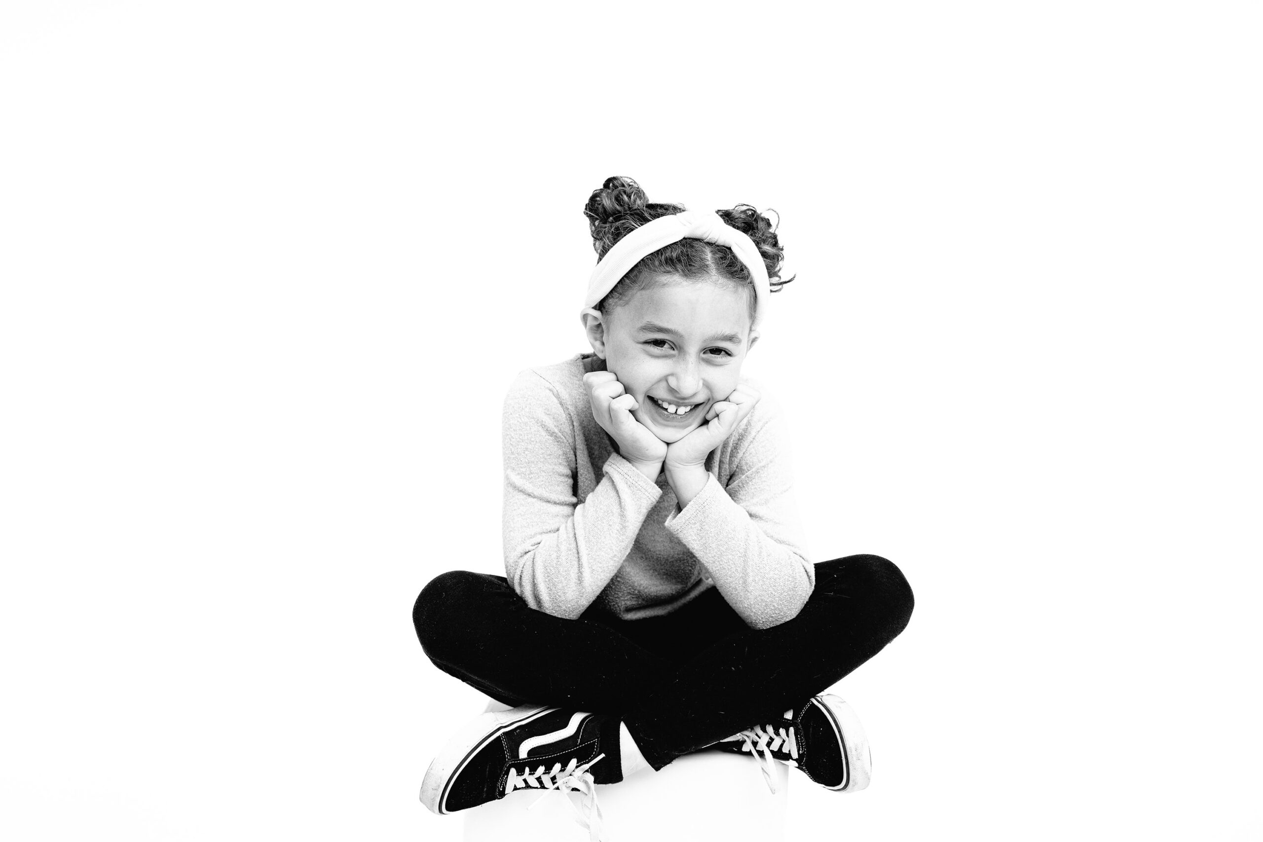 Black and white image of a 10-year-old girl during her personality portrait session with her hands on her chin laughing