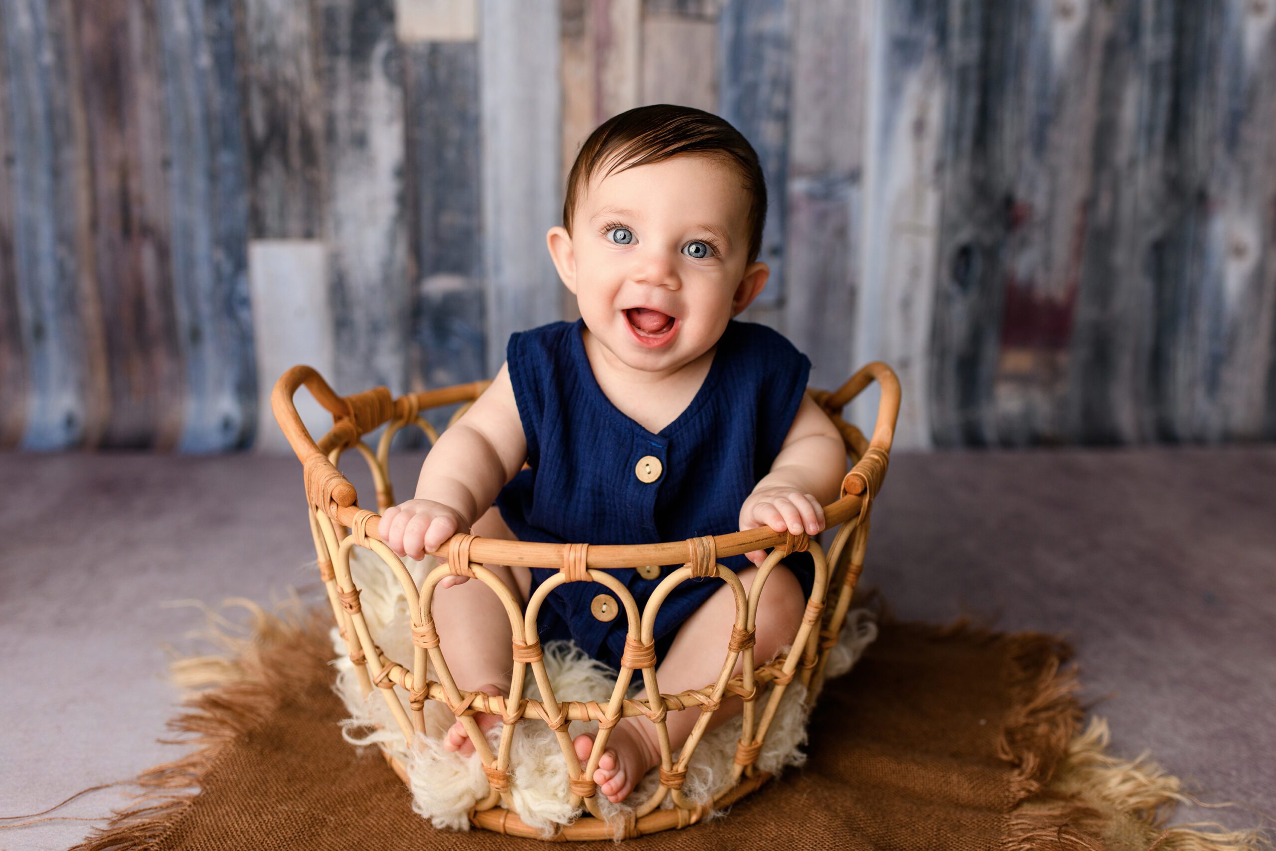 A little boy from Waxhaw sits dressed in blue during his milestone sitter session, smiling back at the camera