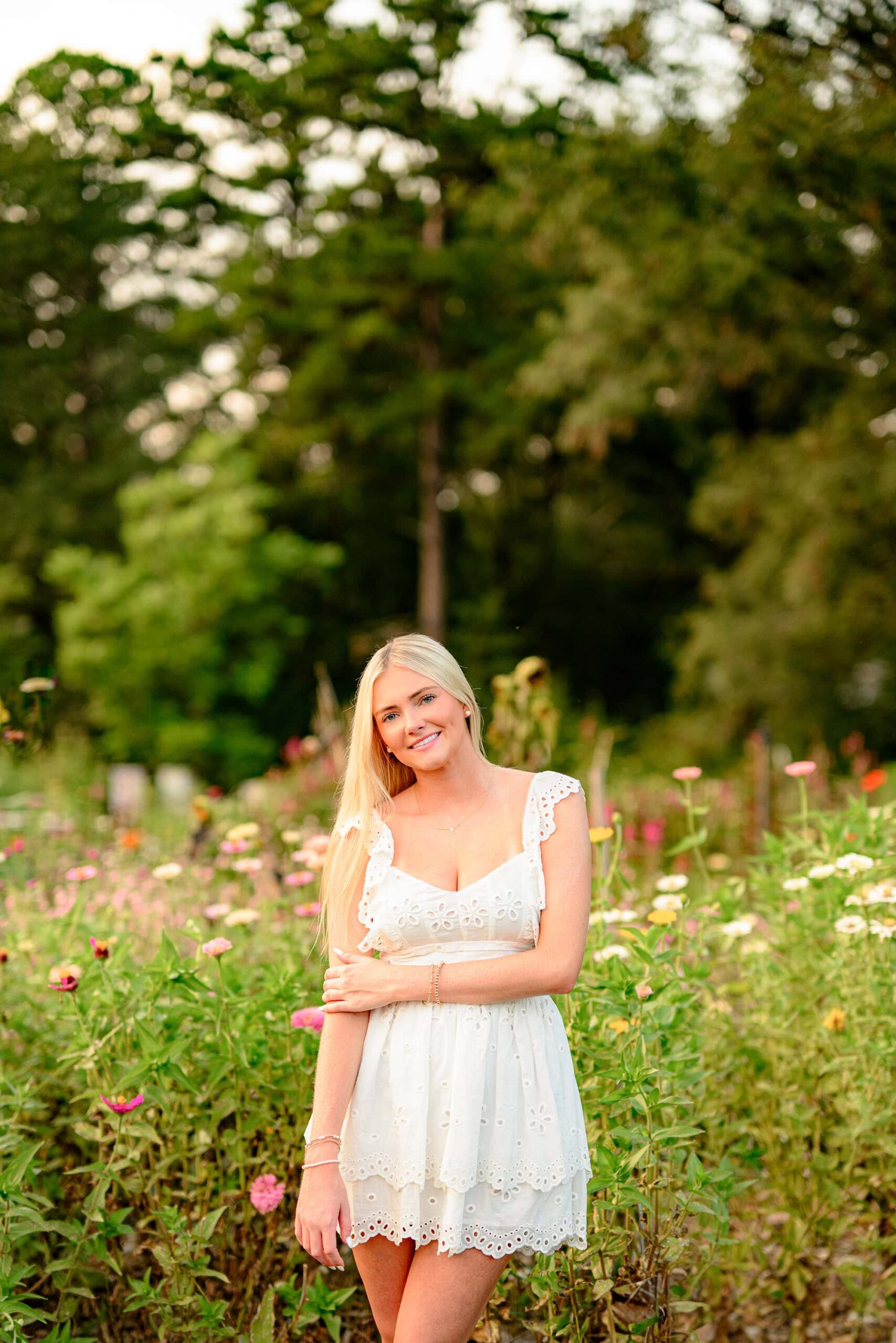 She poses gracefully with one arm draped across her waist, her cream baby doll dress flowing lightly in the breeze. The colorful flower field adds a bright and cheerful ambiance to the scene.