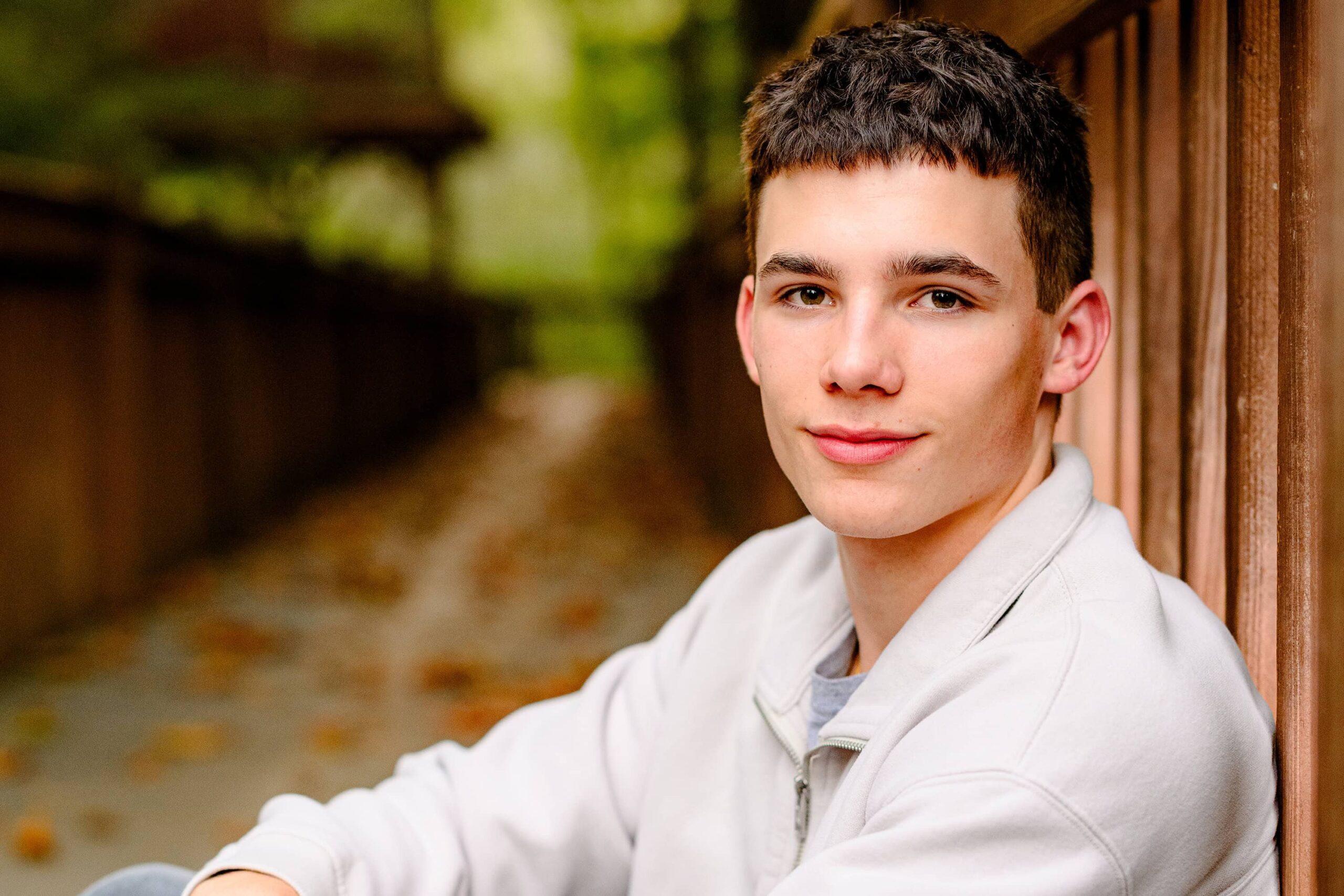 The grad, wearing a relaxed pose, sitting and leaning back against a railing, exuding confidence and strength, set against the peaceful backdrop of nature.
