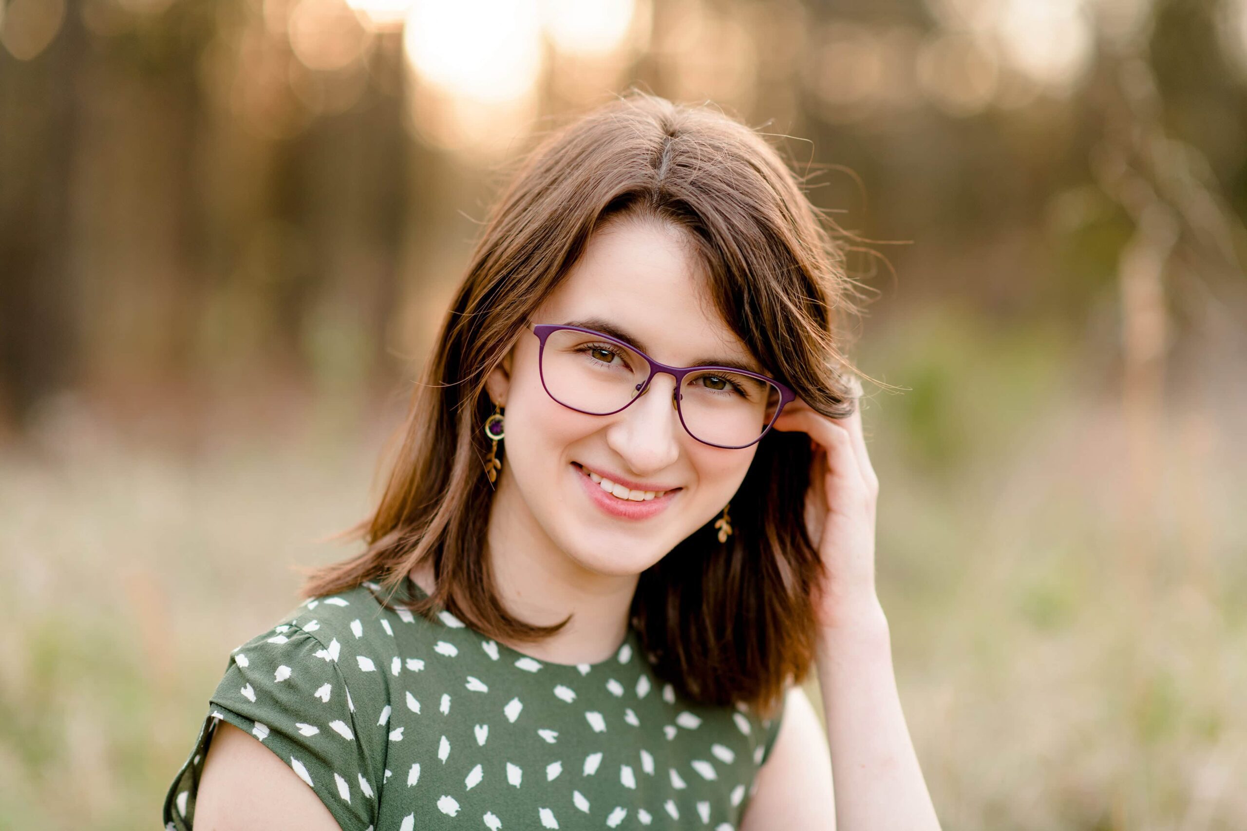 dark hair senior girl wearing a green dress and glasses tucks hair behind her ear