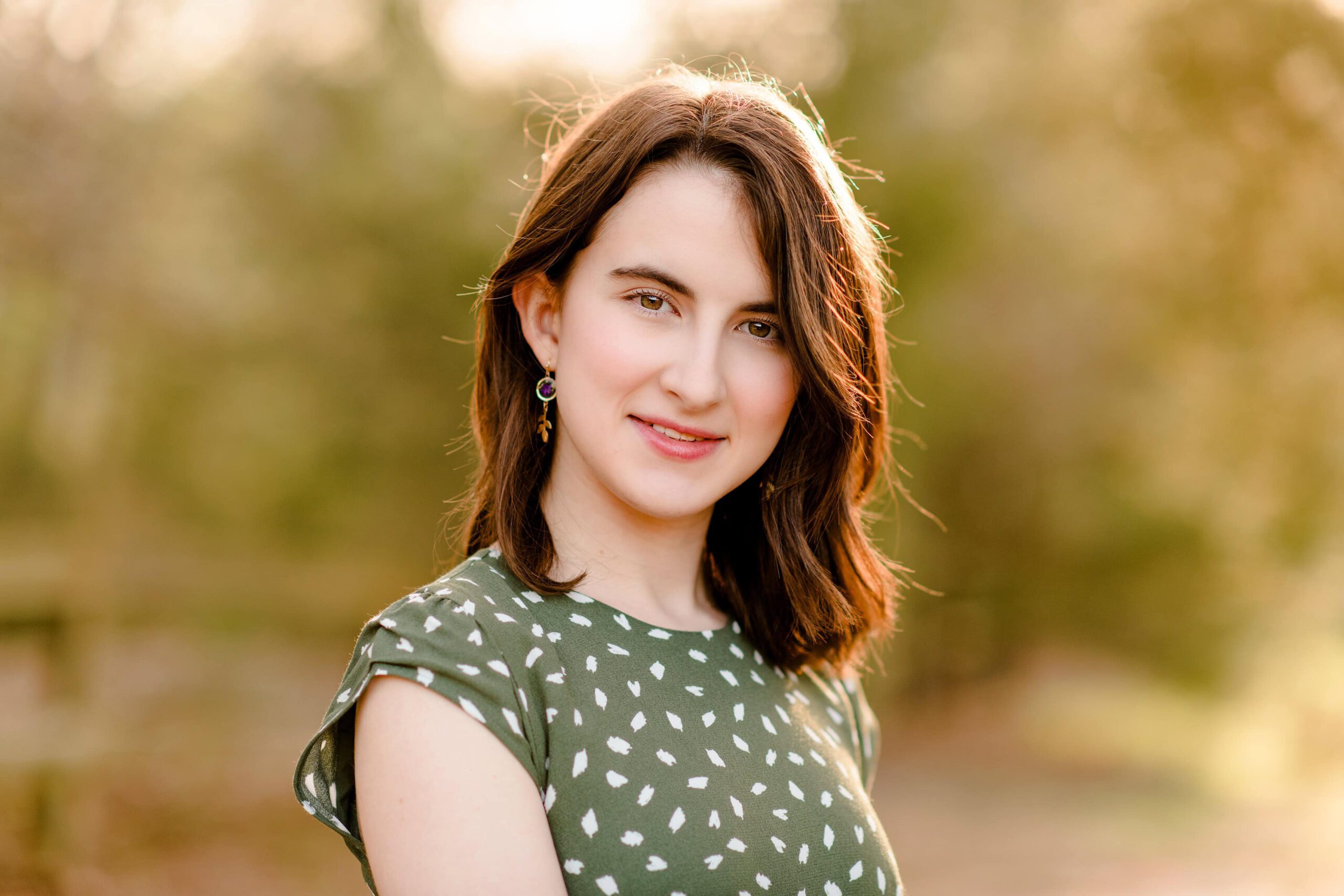 close up portrait of a grad wearing a green dress with golden light on her dark hair