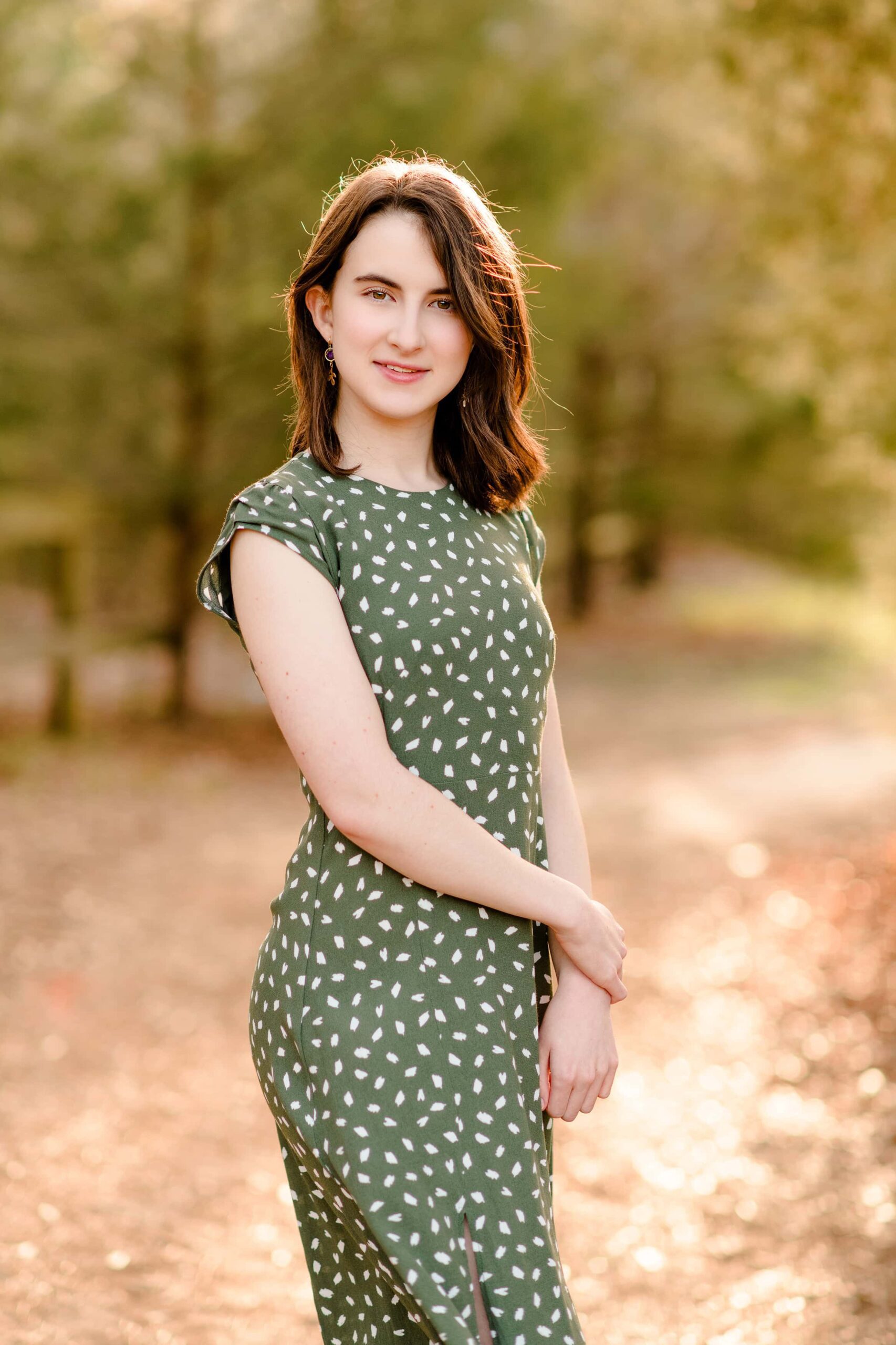 graduate stands in green dress with sun shining behind her