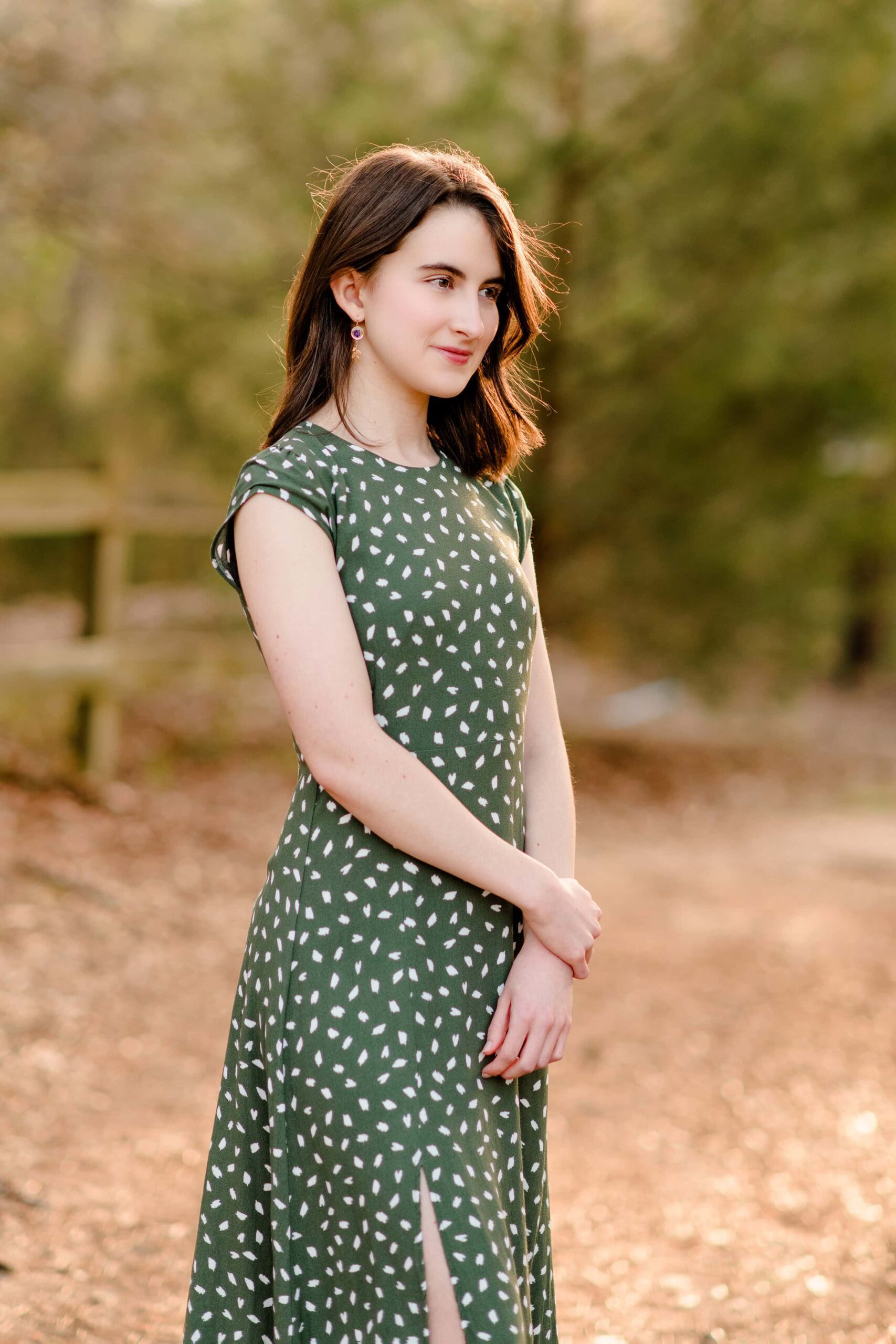 dark hair girl stands with her hands in front of her looking off into the distance