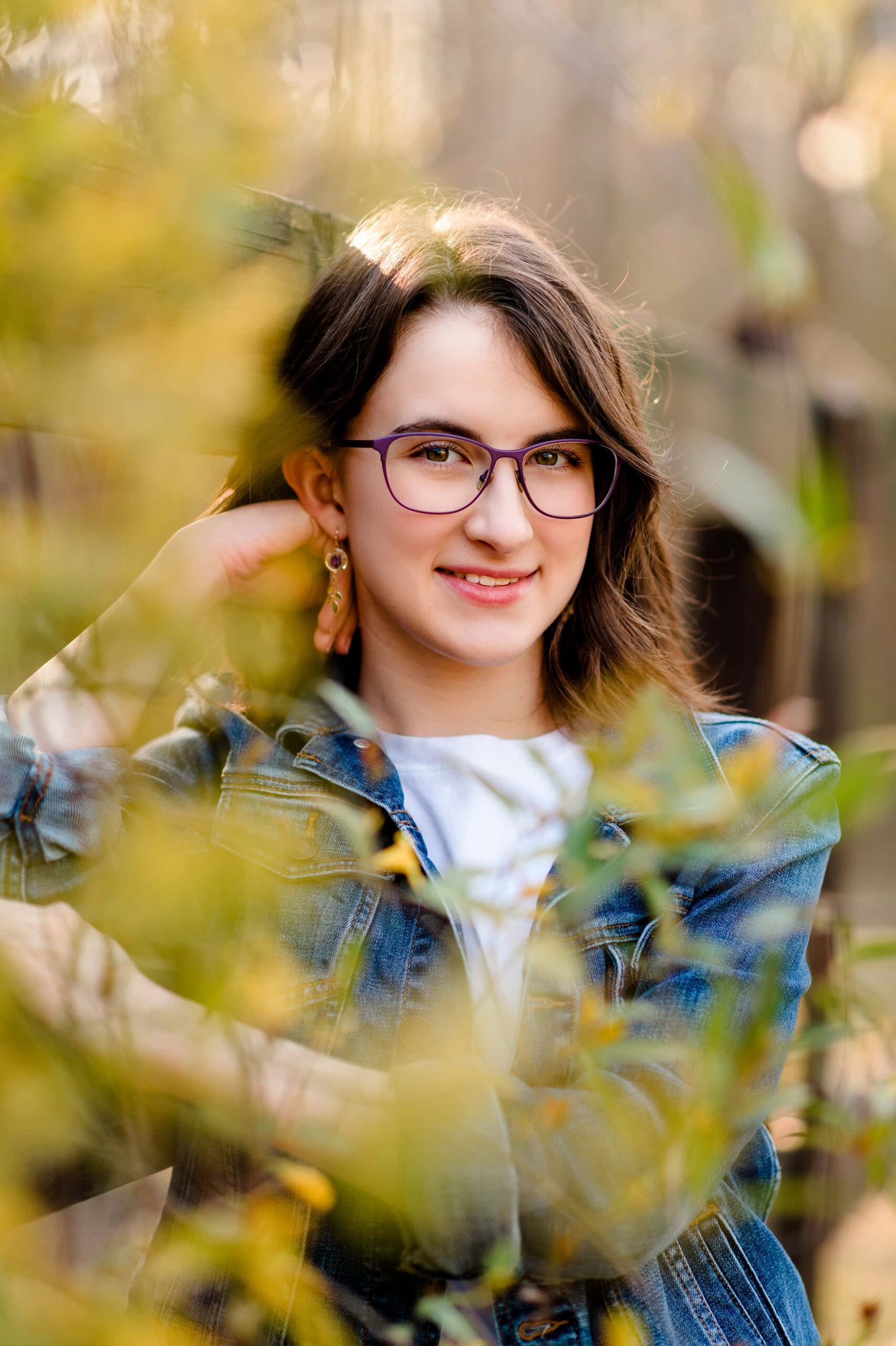 dark hair senior girl in glasses poses behind flowers