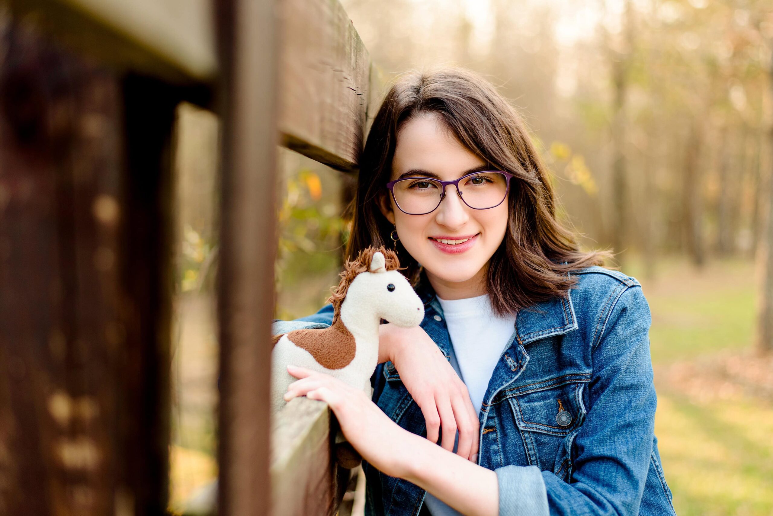 dark hair senior with glasses wearing a jean jacket cuddles her childhood stuffy