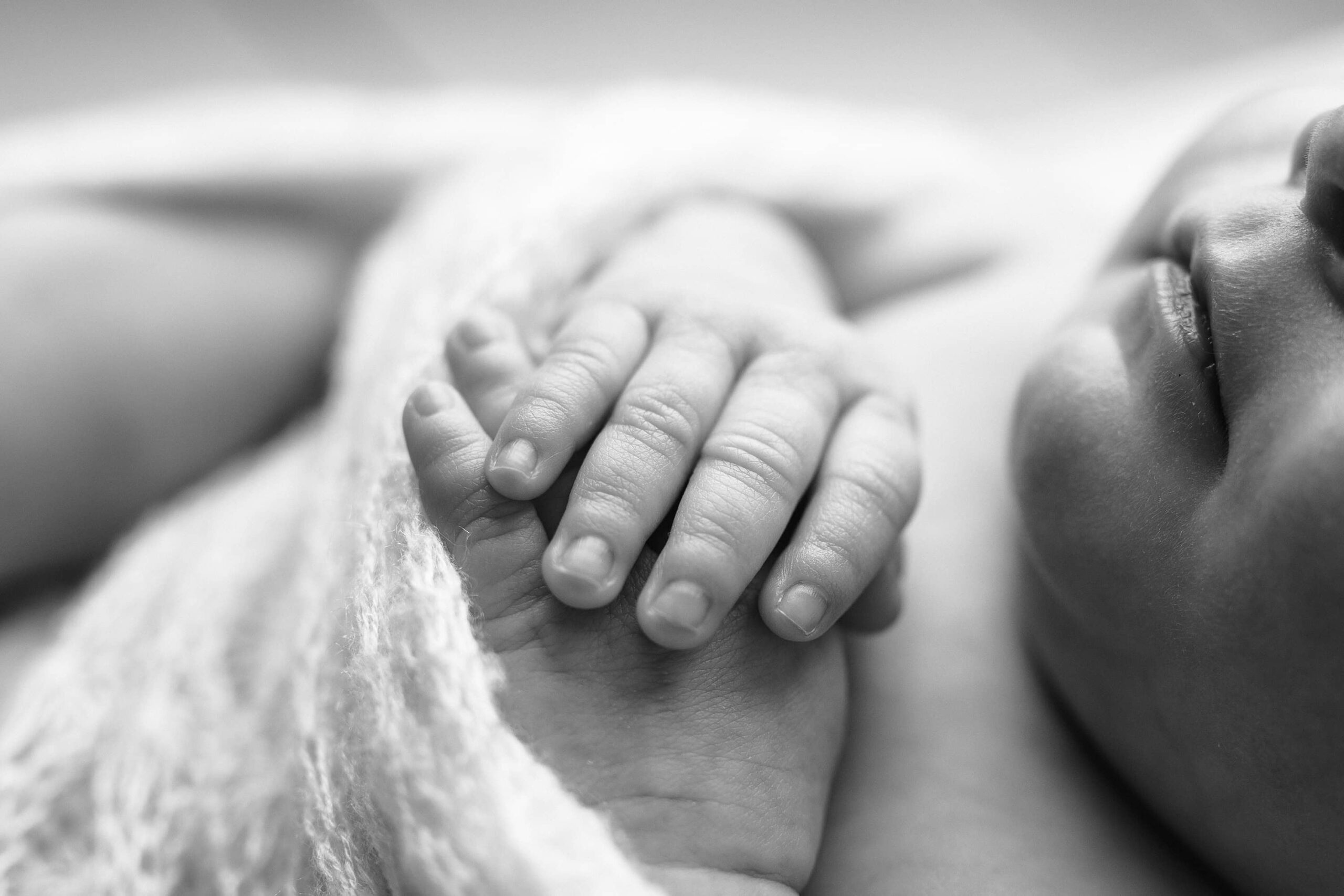 Black and white image of a newborn baby's tiny hands, gently resting in the studio, highlighting the preciousness of her delicate fingers in a Charlotte-based studio.