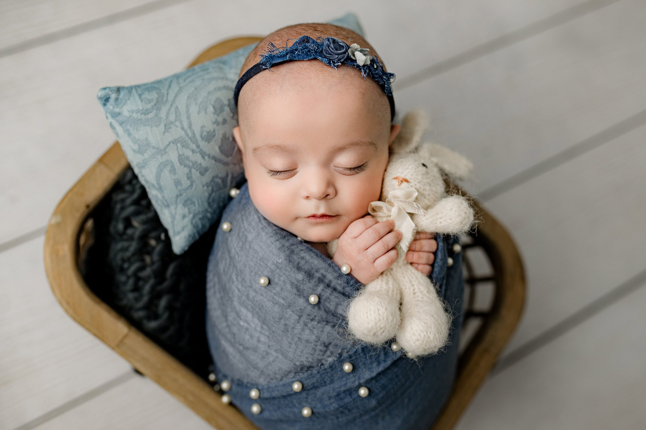 Asleep newborn baby girl, wrapped in blue and snuggling a white stuffed bunny close to her face, captured in the Waxhaw studio for a tender, affordable newborn moment.
