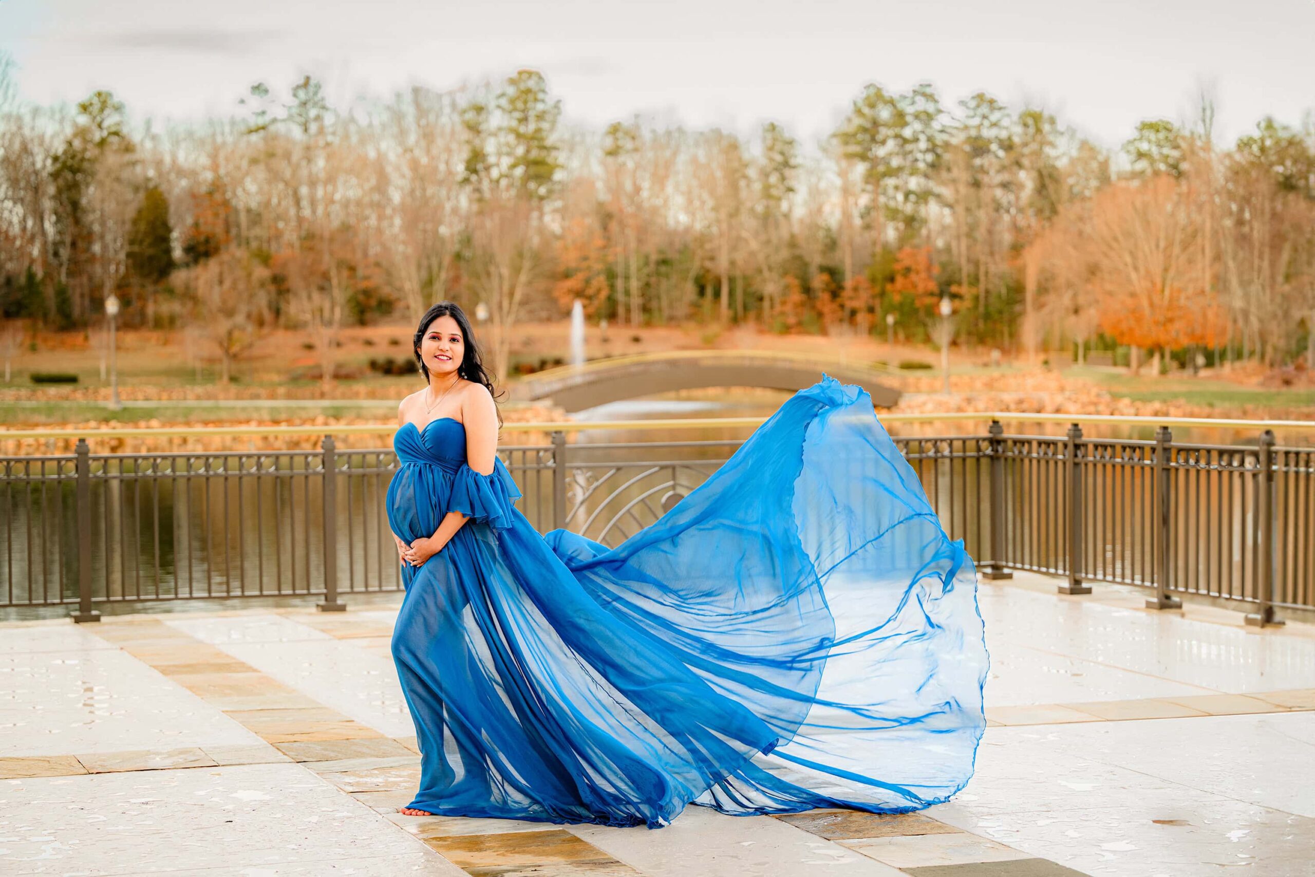 pregnant charlotte nc mother wearing blue dress that is blowing in the wind during her photoshoot