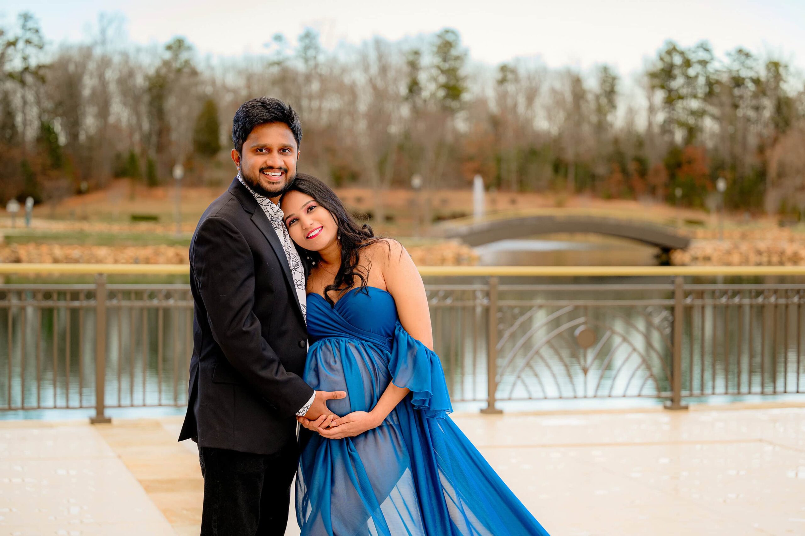 expectant mom in dressed in blue leans against her husband dressed in black during their charlotte maternity photo session