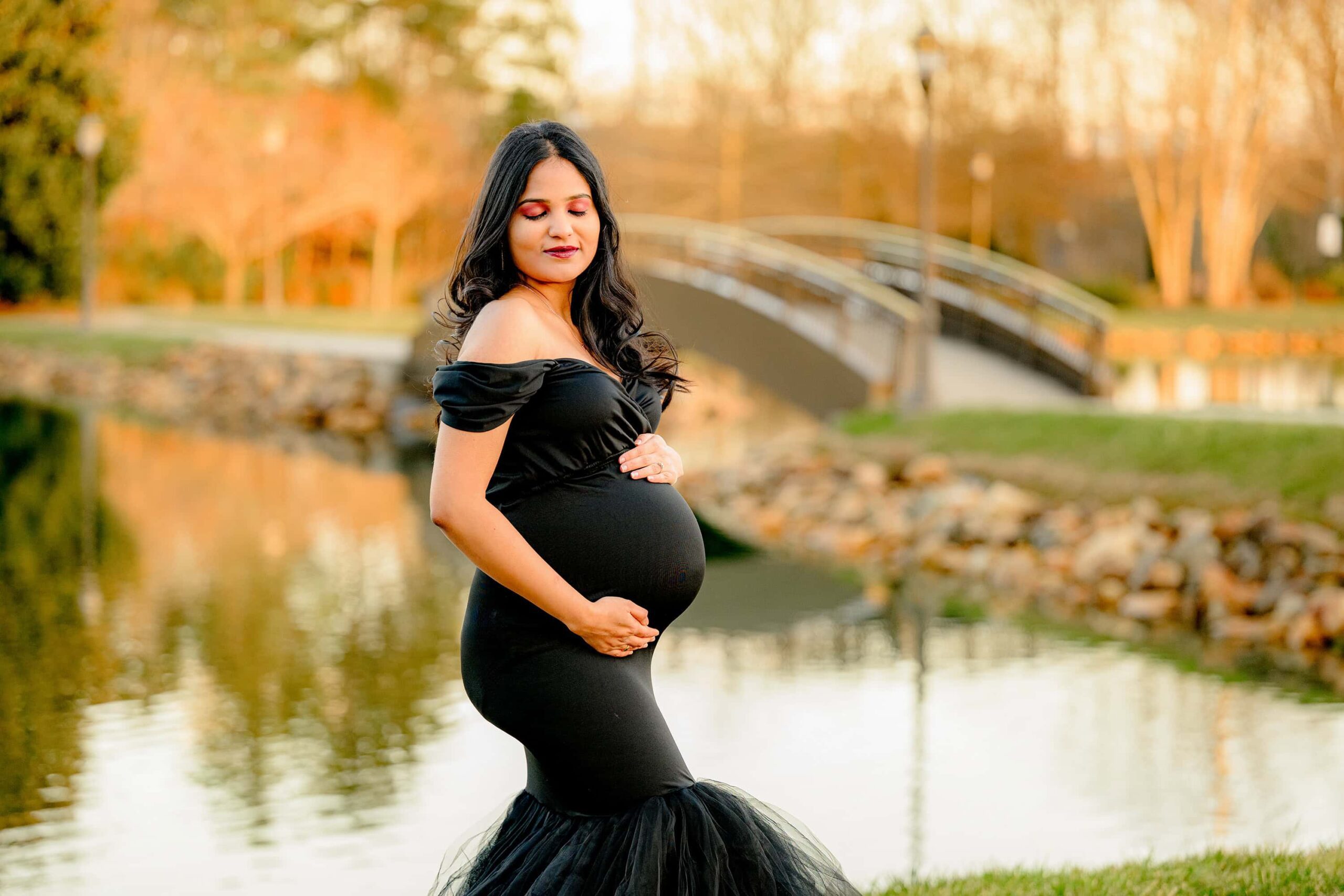 pregnant mother poses in a black dress with a sweetheart neck and both her hands on her belly