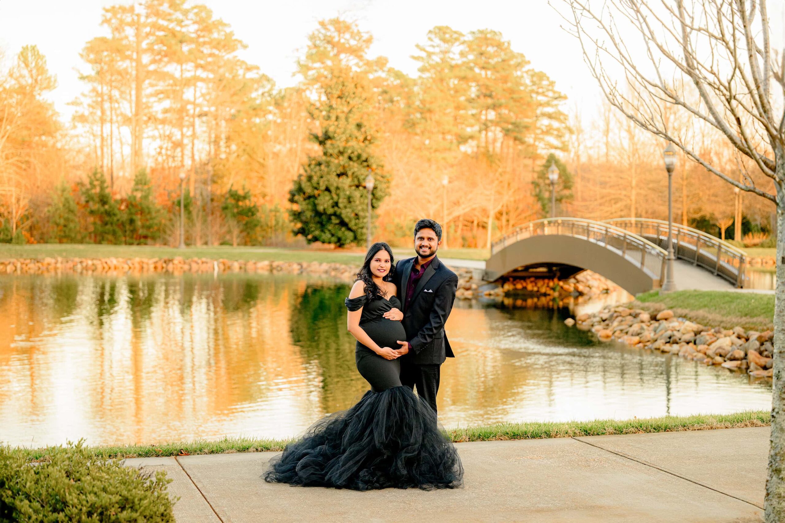 couple poses together with hands on the expectant mother's pregnant belly during golden hour