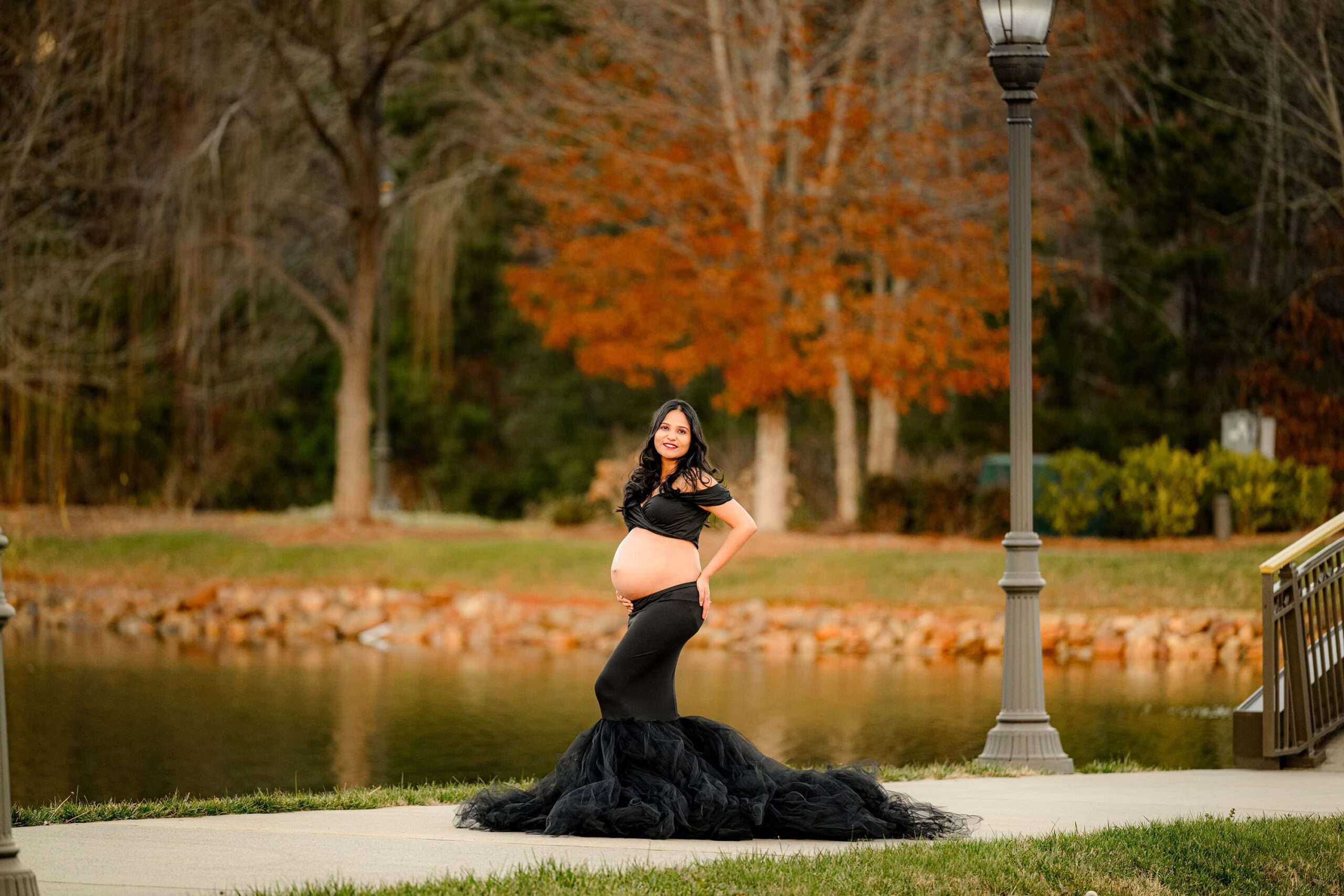 expectant mother poses in a dress with her belly showing and the golden light behind her