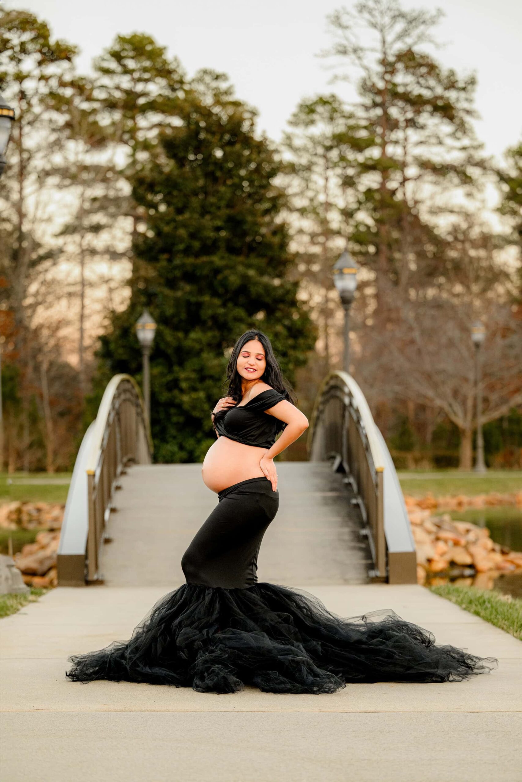 a black tulle dress on this expectant mother shows off her belly while she is posed with her hand in her hair and her other hand on her back hip