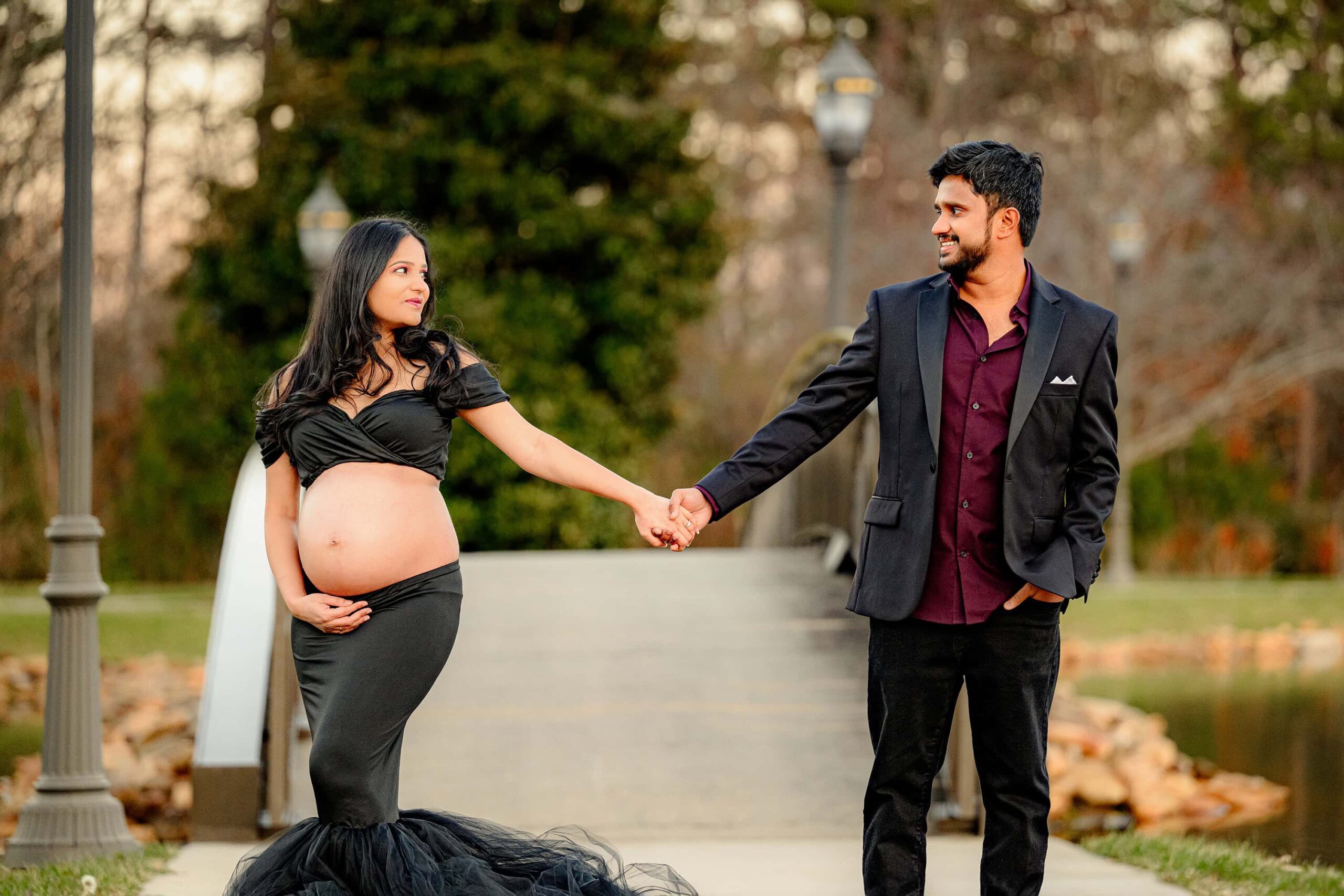 couple stands hand in hand dresses in semi formal - expectant mother in black and dad in maroon shirt and coat