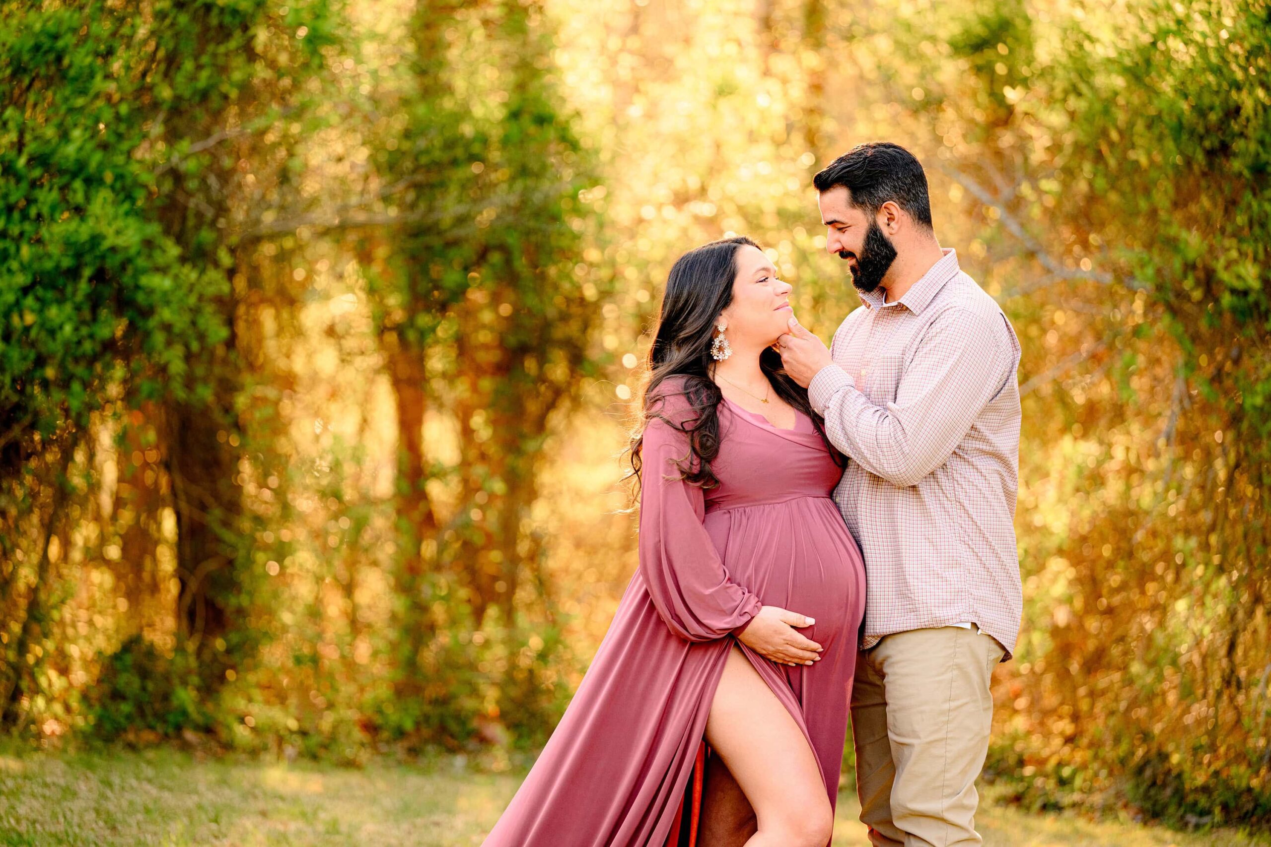 dad is touching mom's chin as she cradles her baby bump while the golden light pours down in this local charlotte area park
