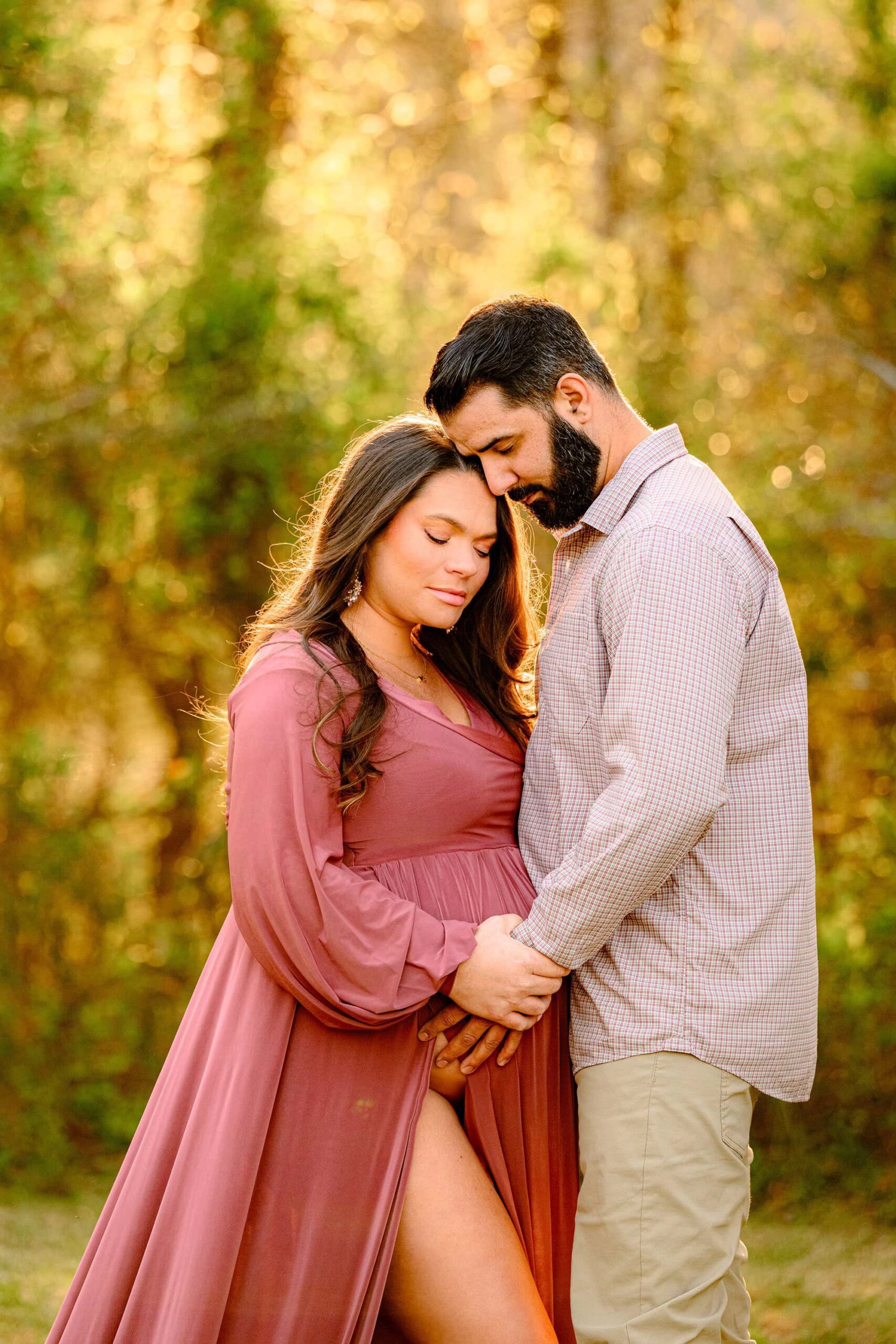 a charlotte expectant couple leans together foreheads touching while looking down at moms expectant belly